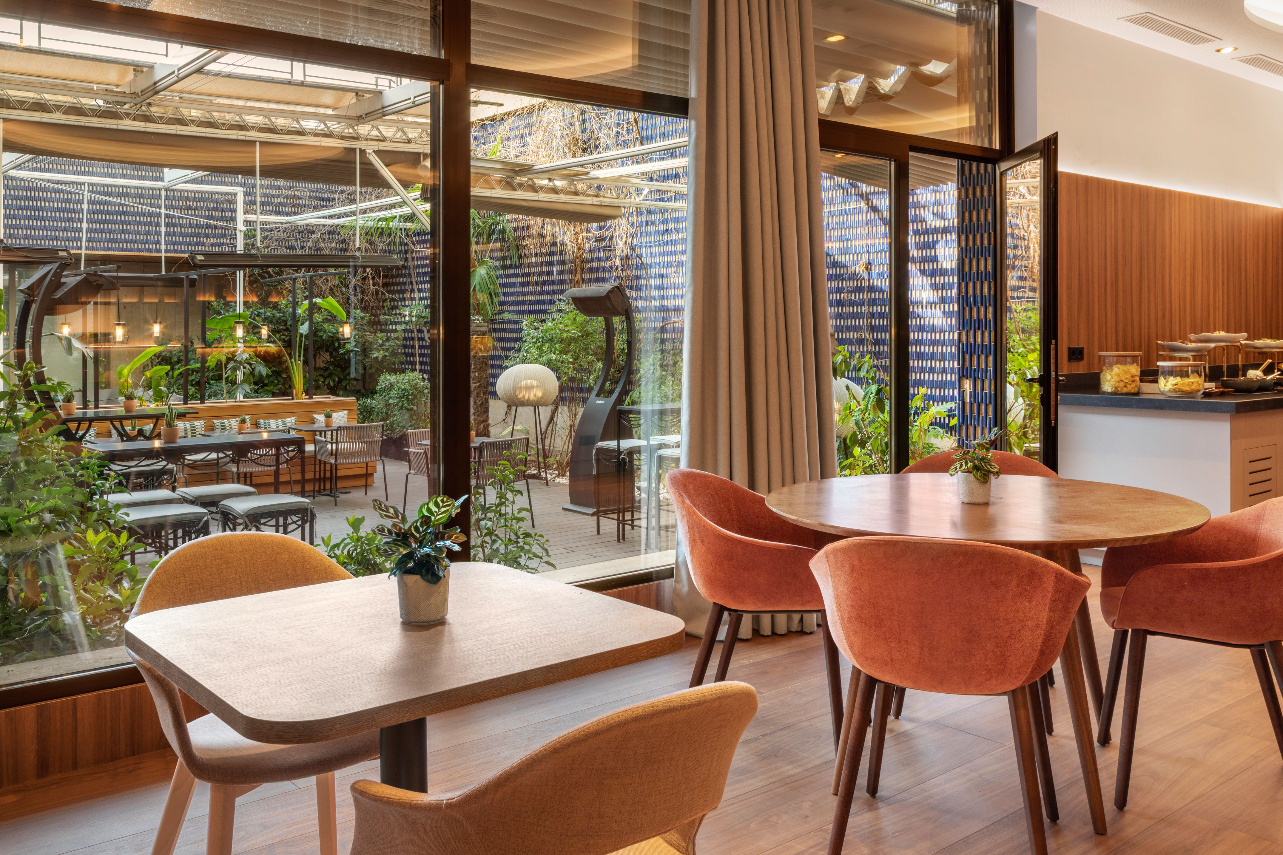 Restaurant interior with modern decor, orange chairs, and green outdoor terrace.