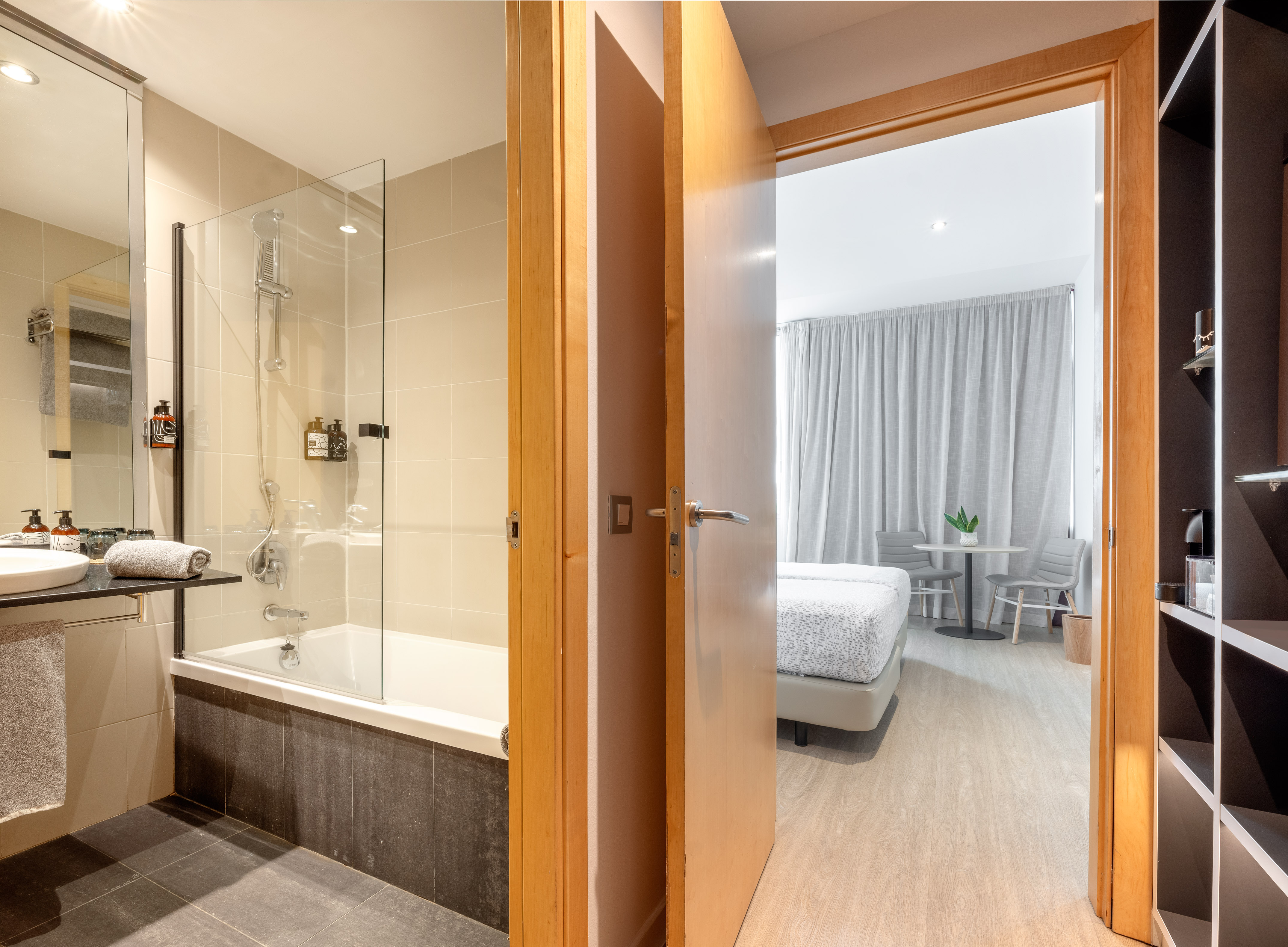 Modern hotel bathroom with shower-tub combo, connecting to a bright bedroom.