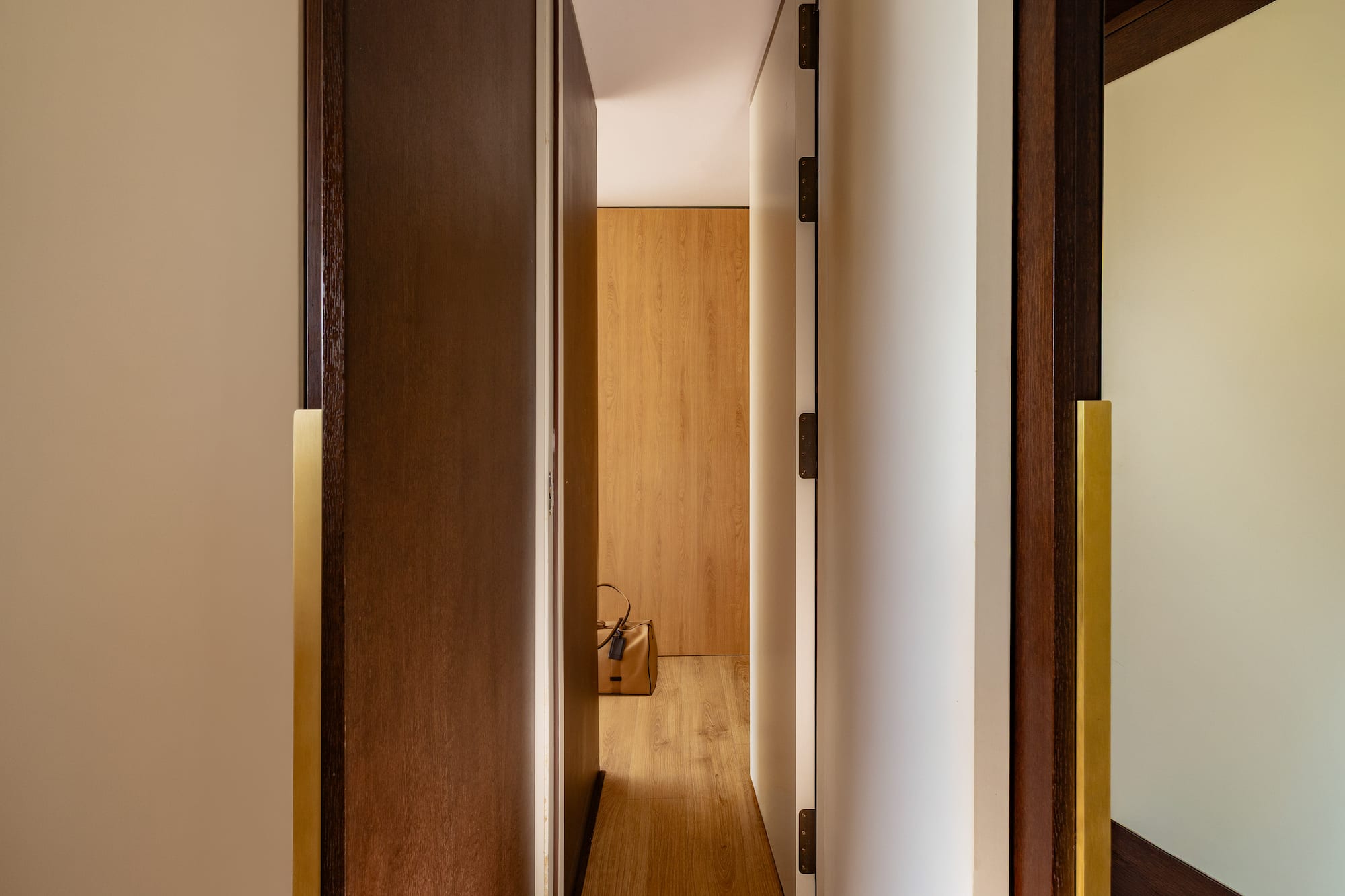 Modern hallway with open wooden doors, brass handles, and a brown bag on light wood floor.