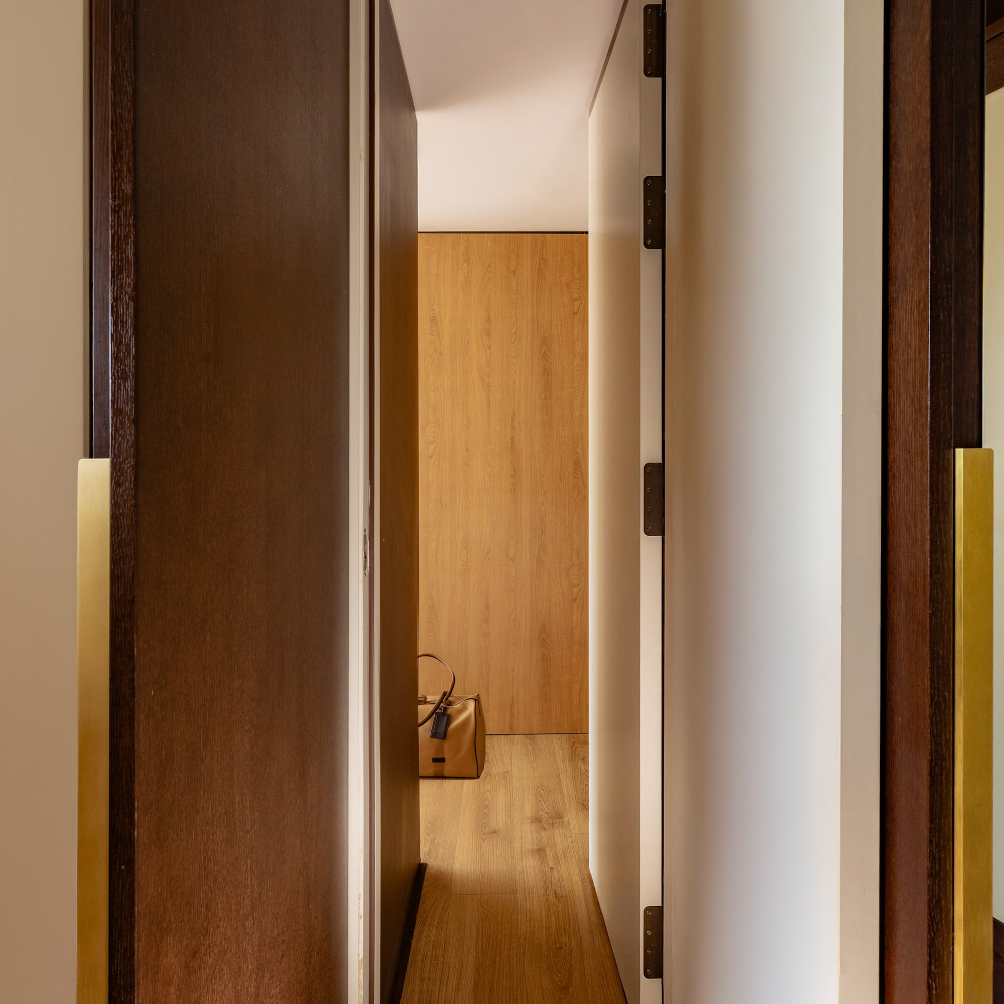Modern hallway with open wooden doors, brass handles, and a brown bag on light wood floor.