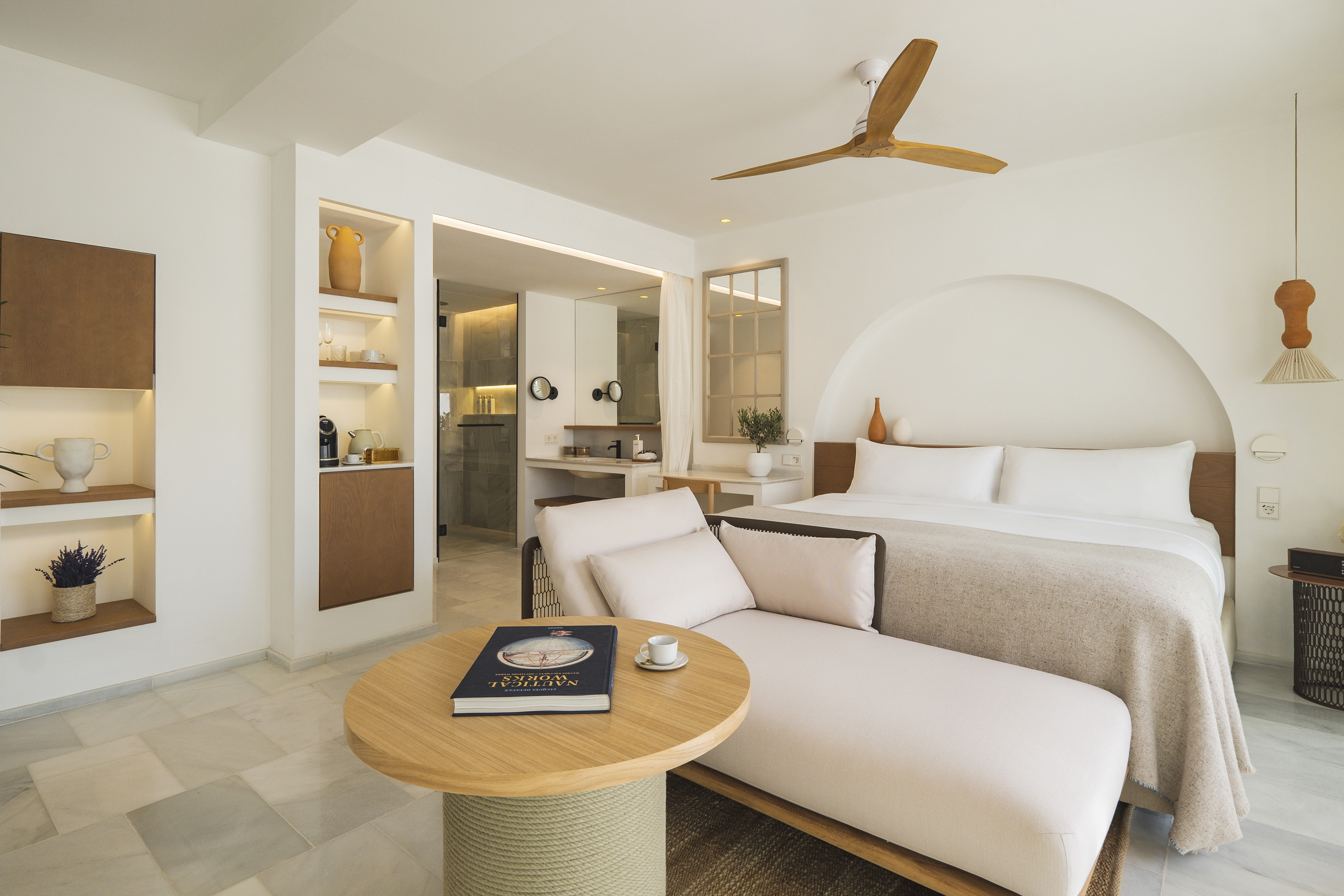 Bright minimalist hotel suite with bed, chaise lounge, and natural wood details.