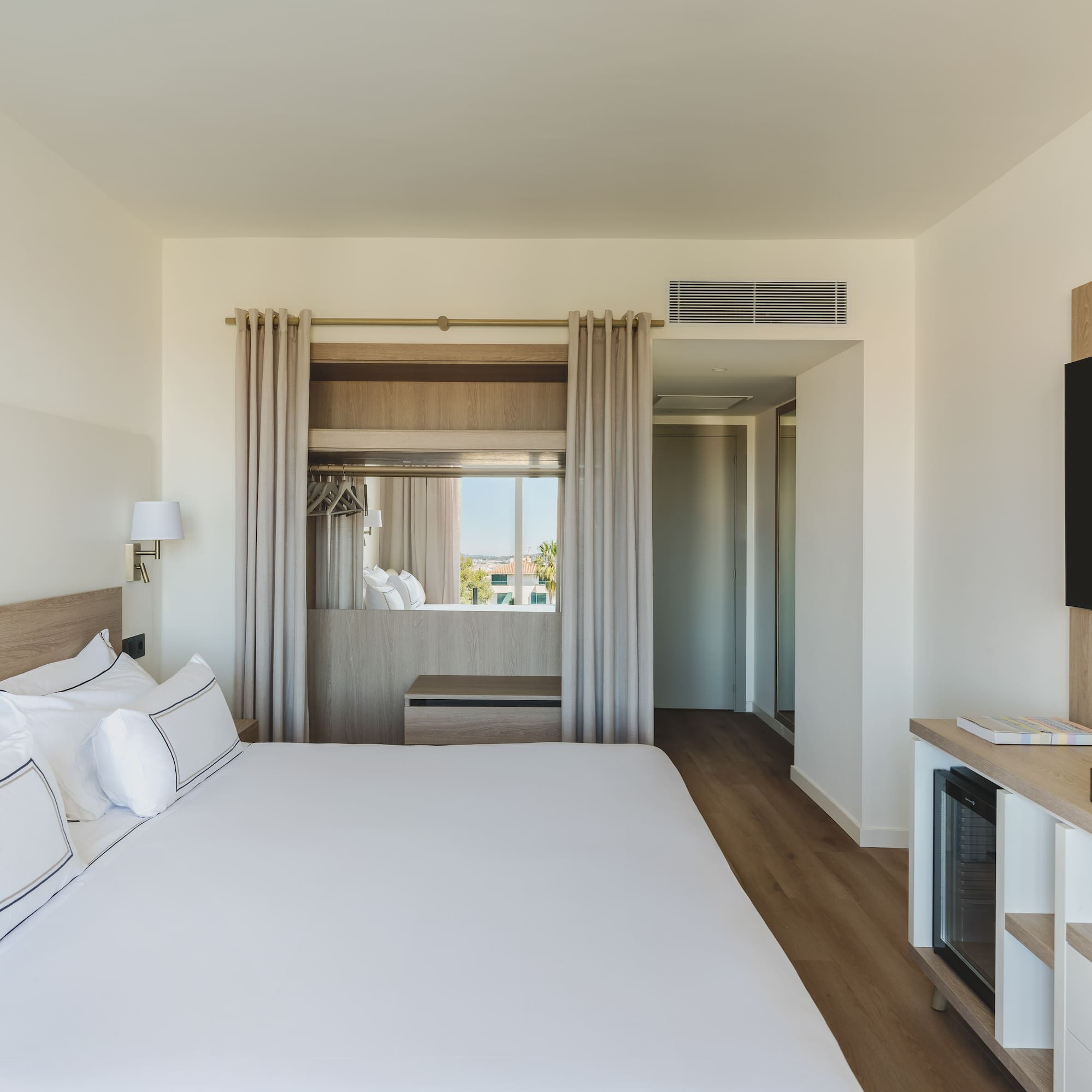 Habitación de hotel moderna con cama grande, TV y ventanal luminoso.
