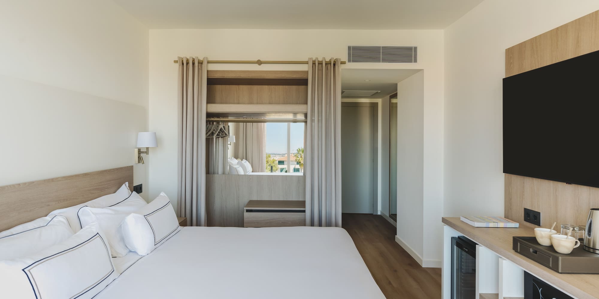 Habitación de hotel moderna con cama grande, TV y ventanal luminoso.