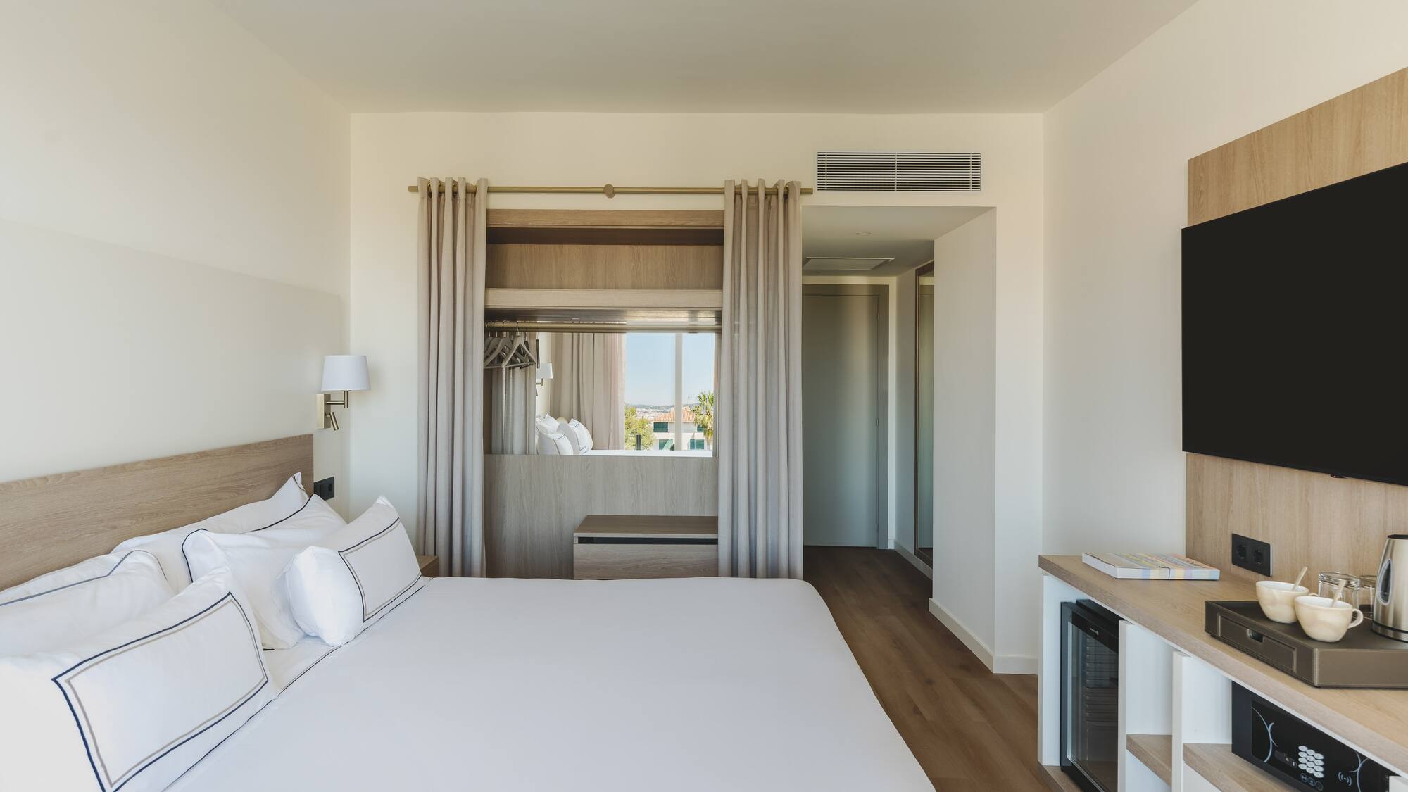 Habitación de hotel moderna con cama grande, TV y ventanal luminoso.