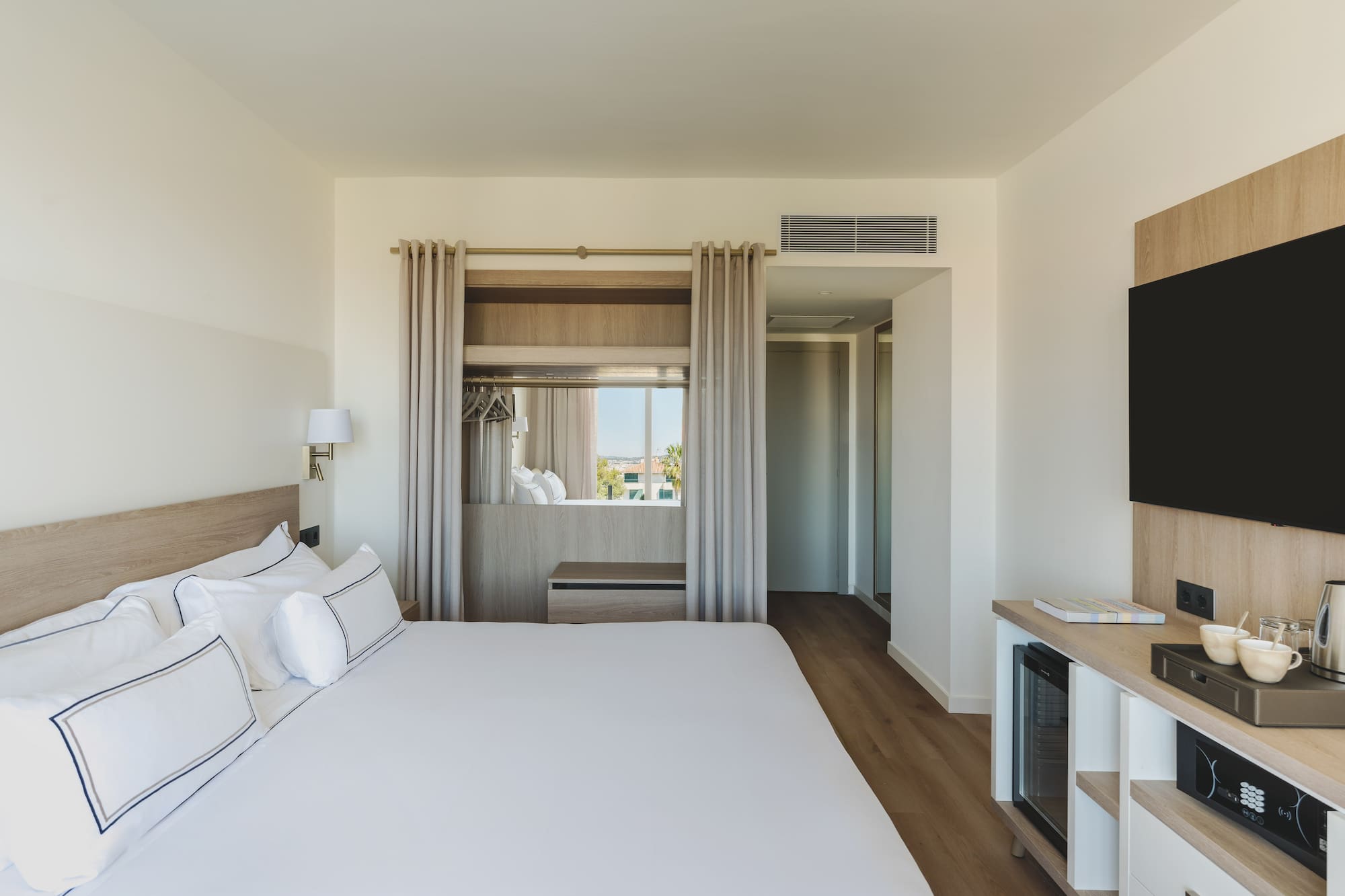 Habitación de hotel moderna con cama grande, TV y ventanal luminoso.