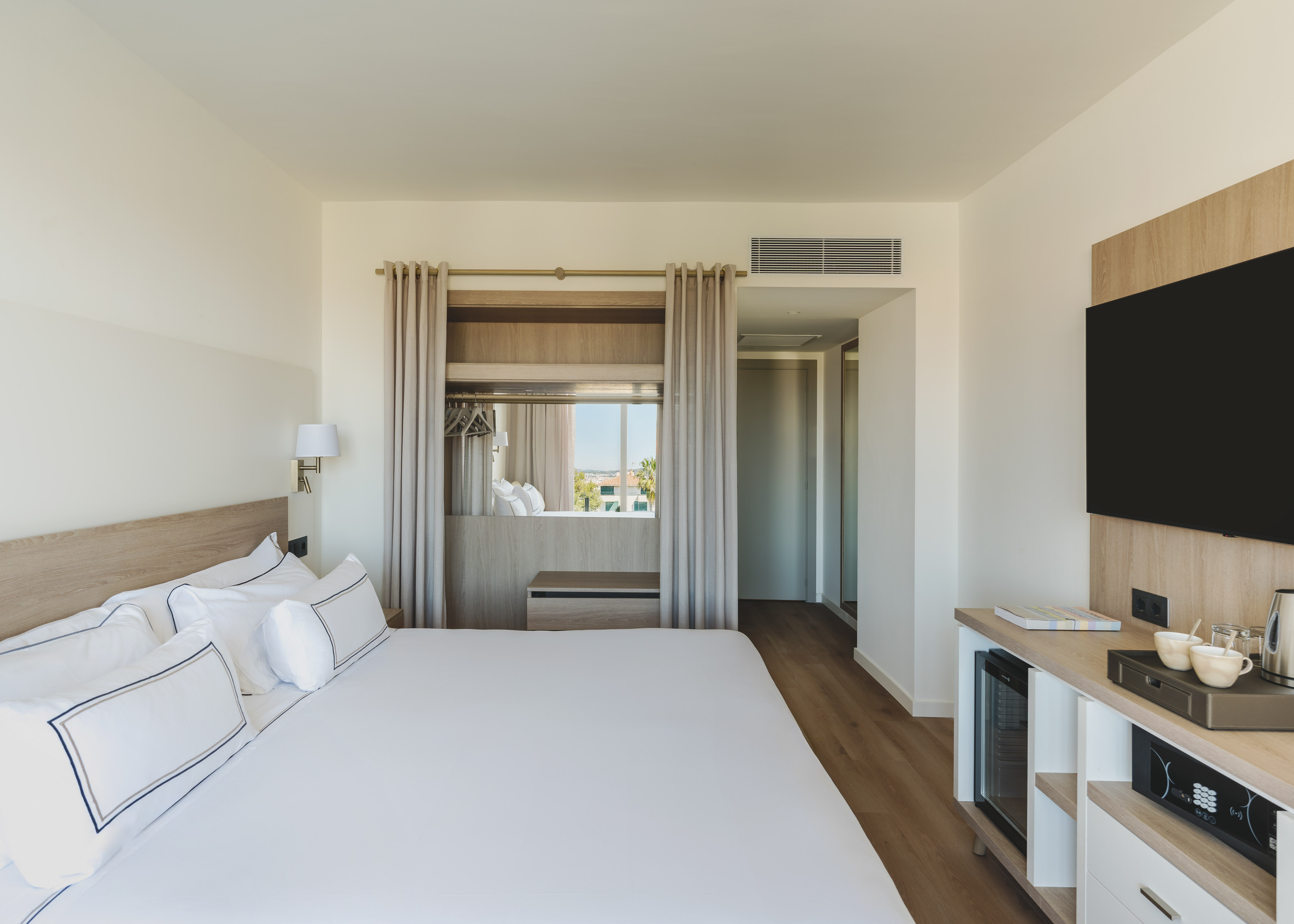 Habitación de hotel moderna con cama grande, TV y ventanal luminoso.