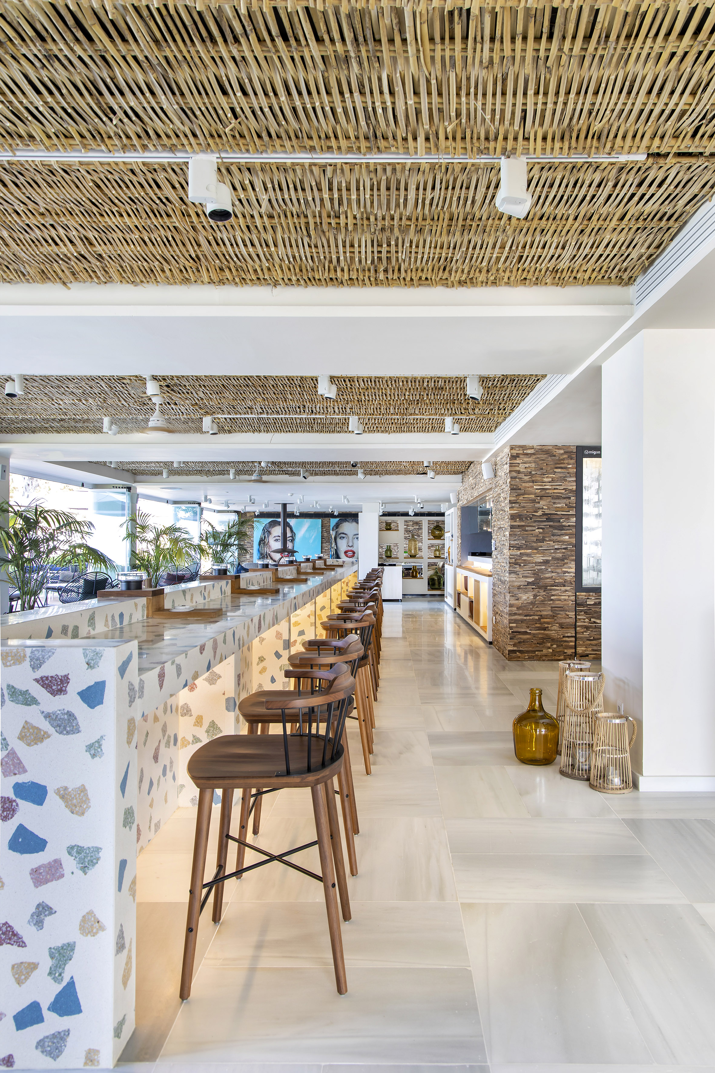 Modern bar with terrazzo counter, bamboo ceiling, and wooden stools.