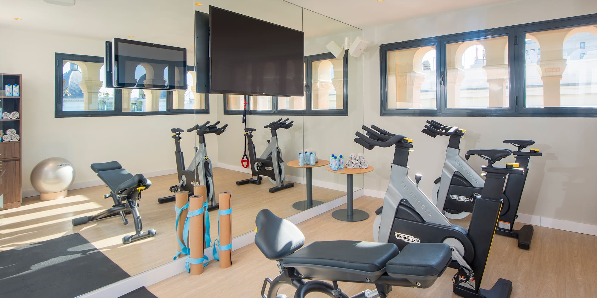 Bright hotel fitness center with spin bikes, workout bench, and large mirrors.