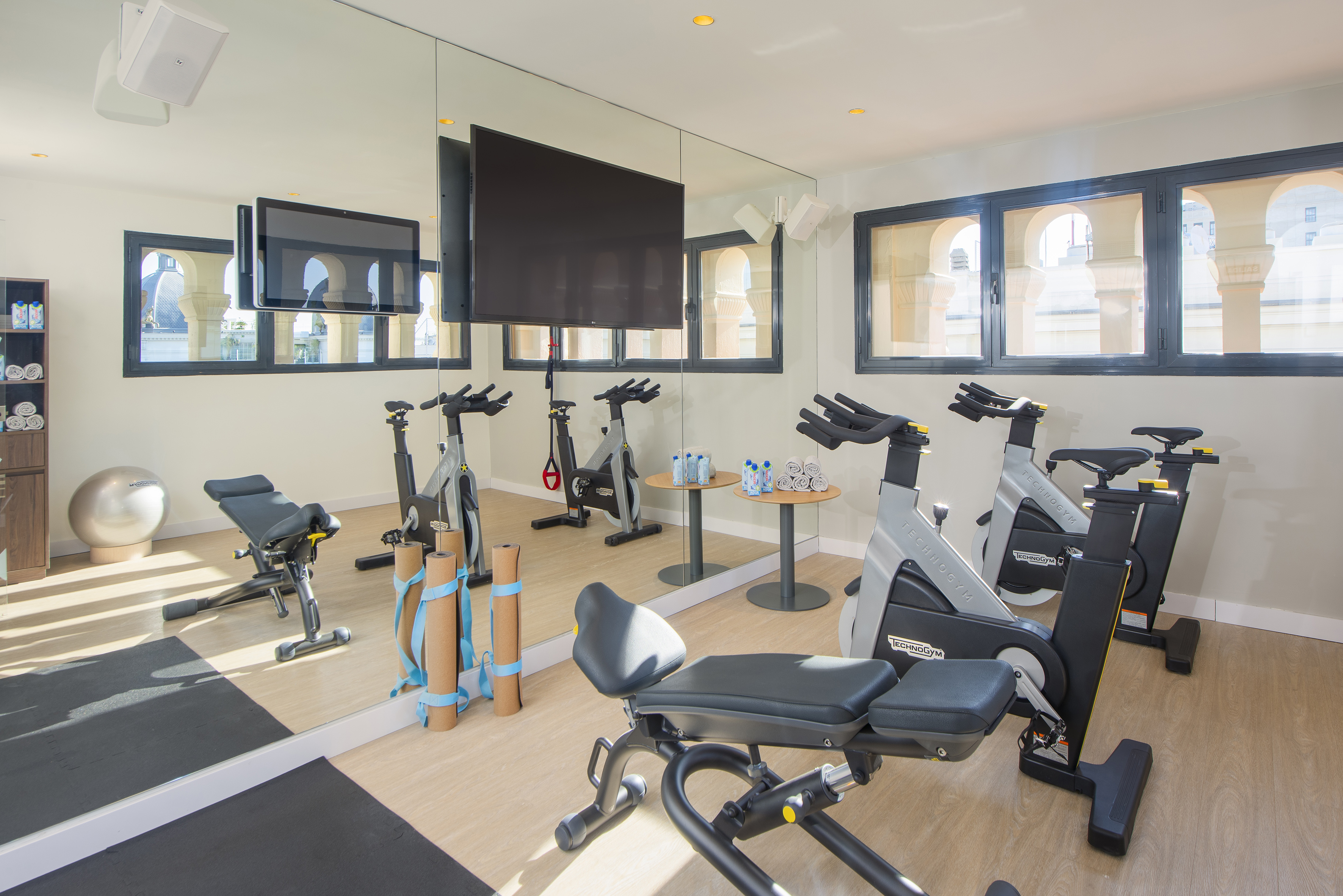 Bright hotel fitness center with spin bikes, workout bench, and large mirrors.