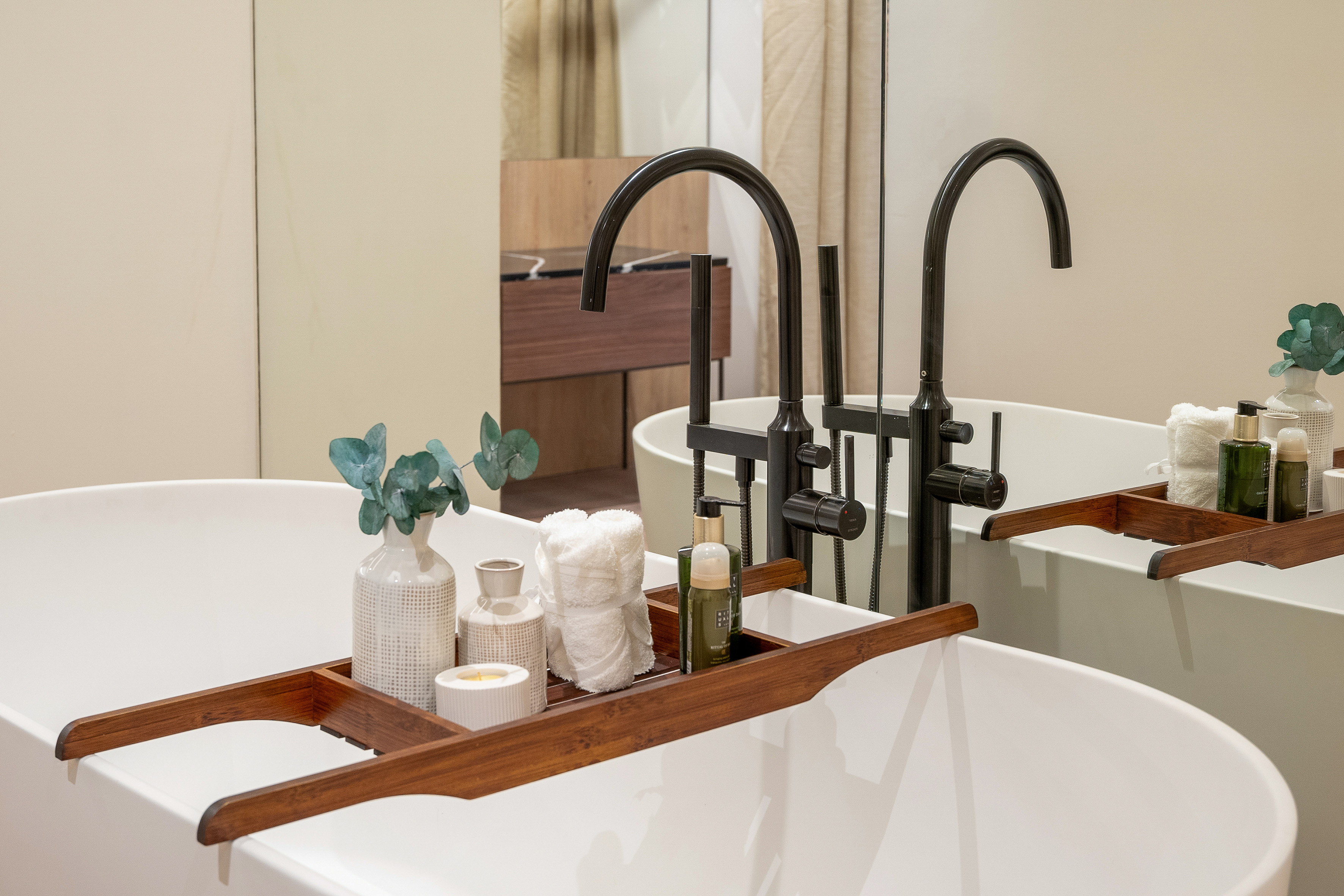 Modern freestanding bathtub with bath caddy, eucalyptus, products, black faucet.