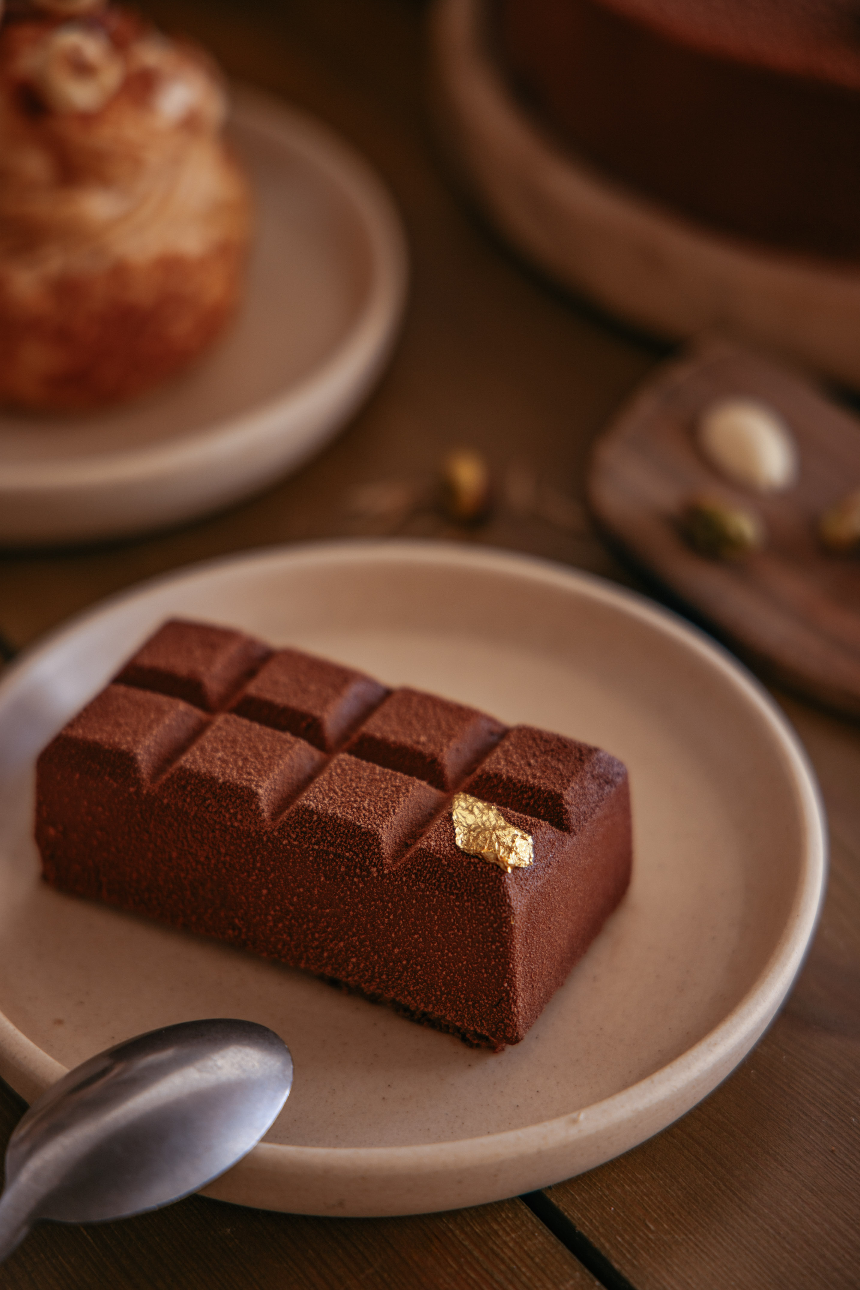Gourmet chocolate bar dessert with gold leaf, cocoa dusted, on a ceramic plate.