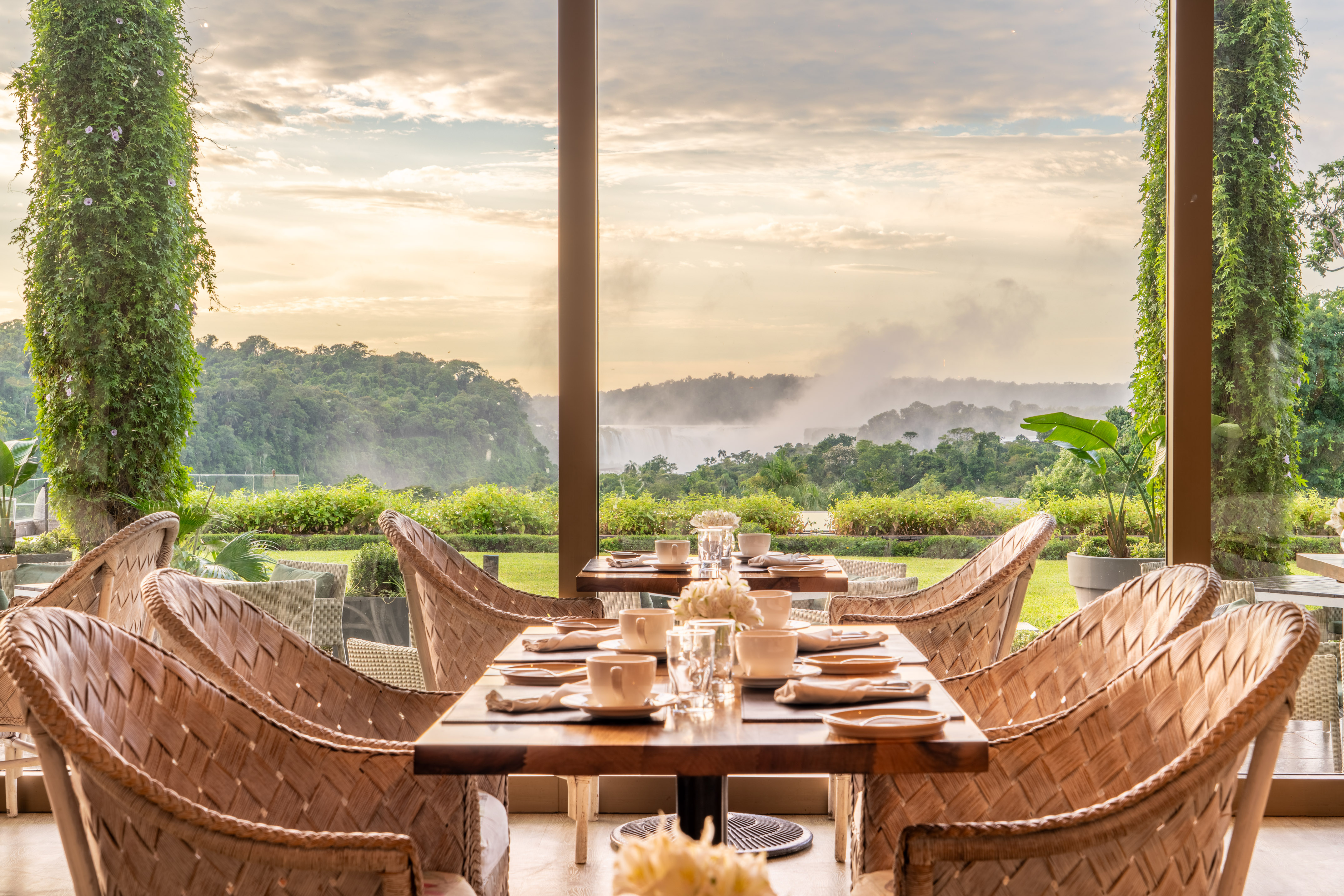 Wicker restaurant chairs and tables with misty jungle waterfall view.