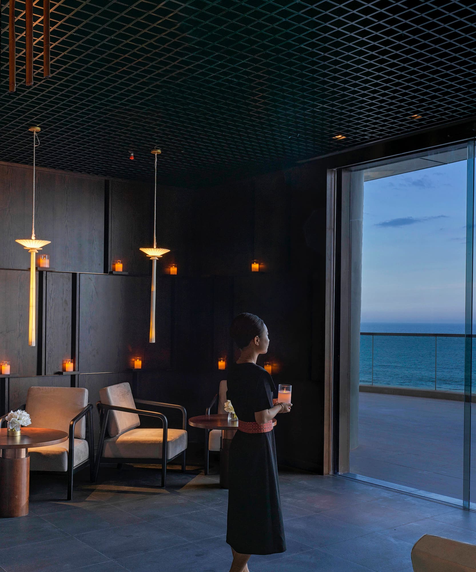 a woman holding a drink in a room with a large window overlooking the ocean