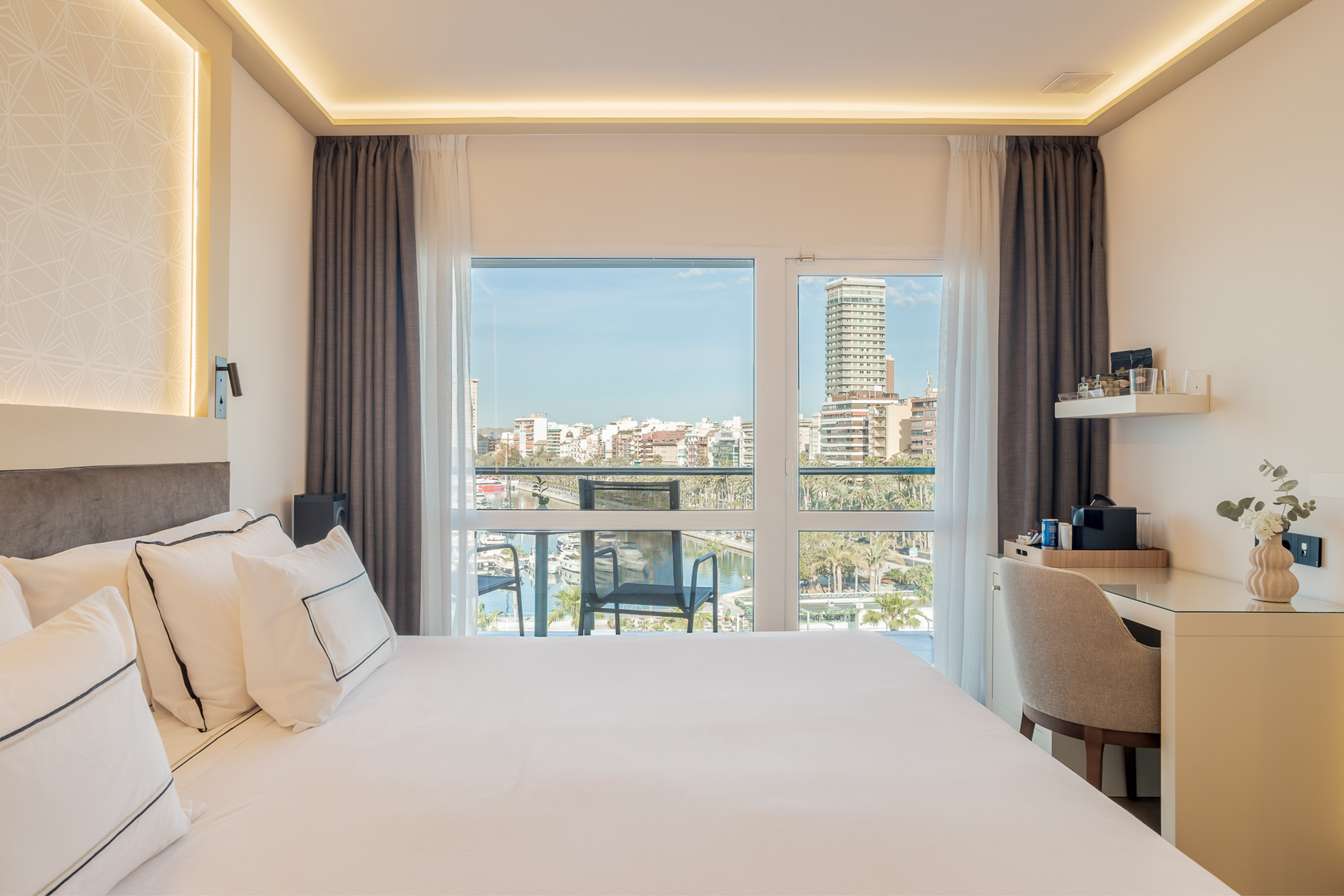 Bright hotel room with expansive marina city view, white bed, desk.