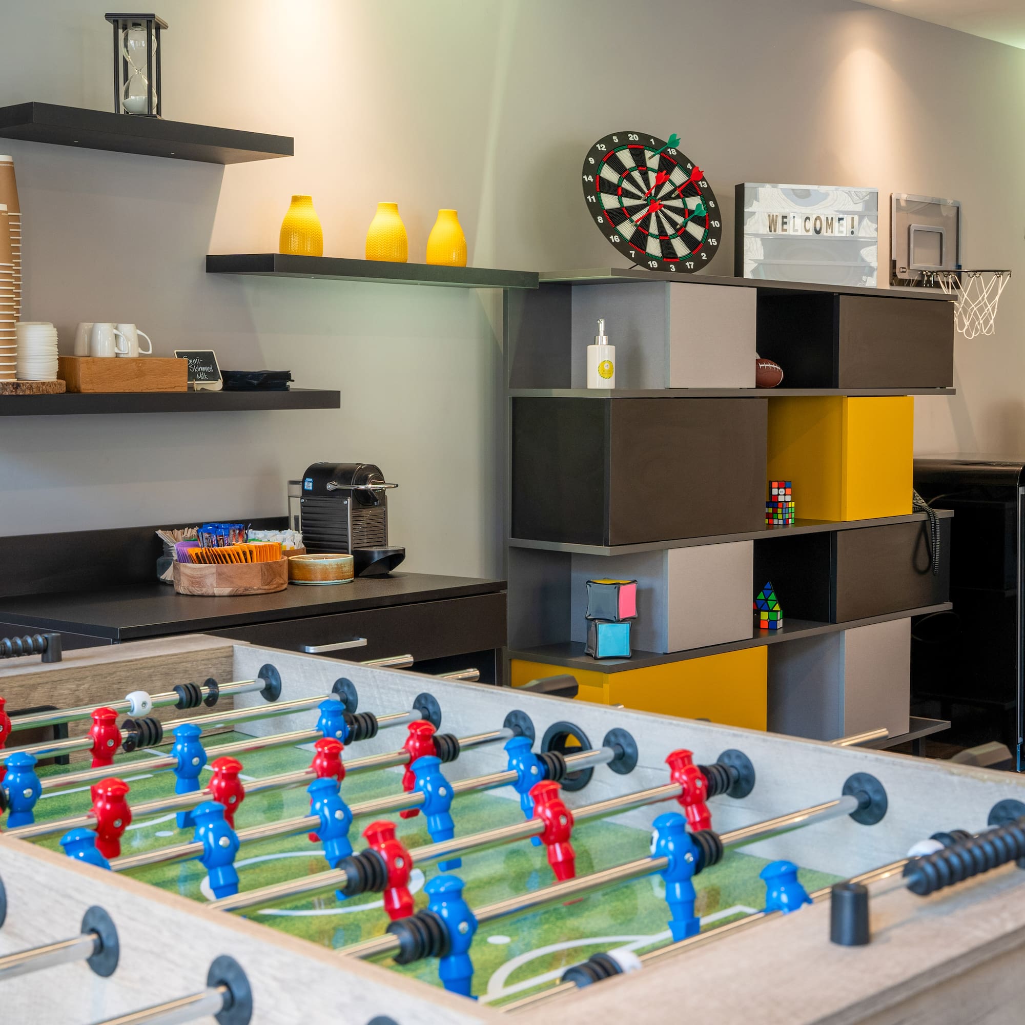 Modern break room with foosball table, dartboard, and coffee station.