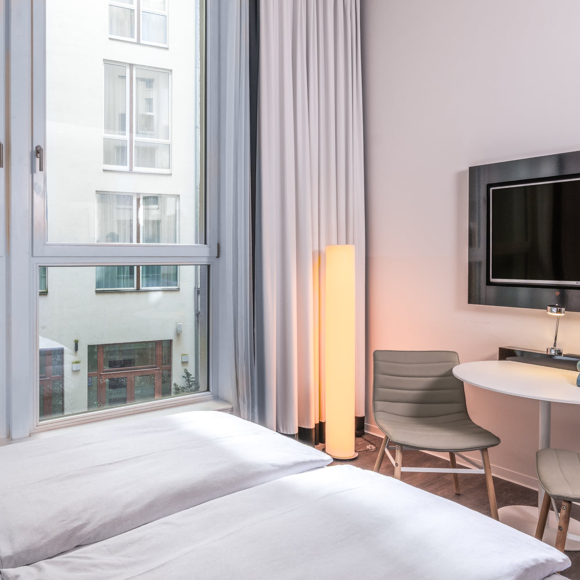 Modern hotel room with bed, window, wall TV, small table, and retro phone.
