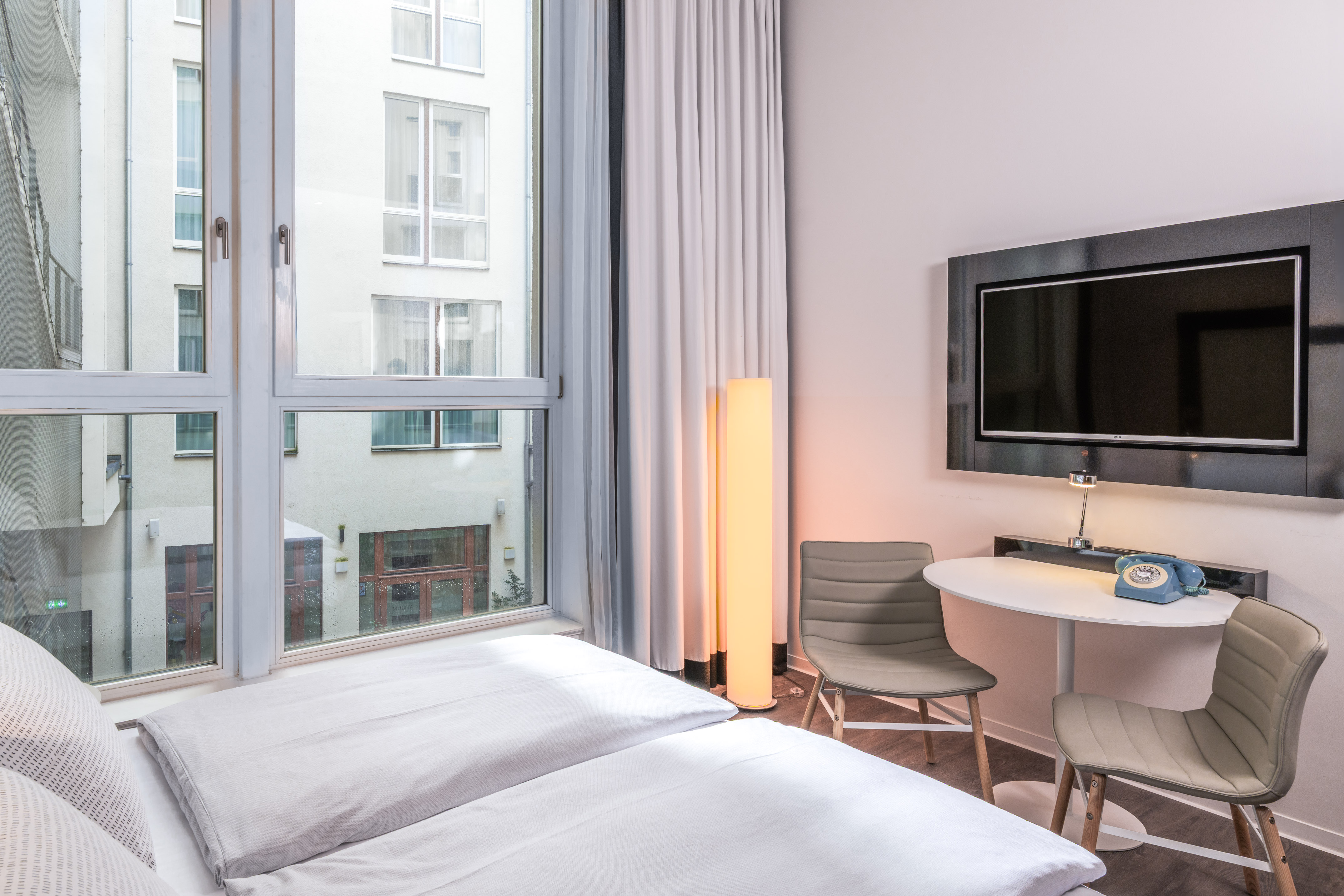 Modern hotel room with bed, window, wall TV, small table, and retro phone.