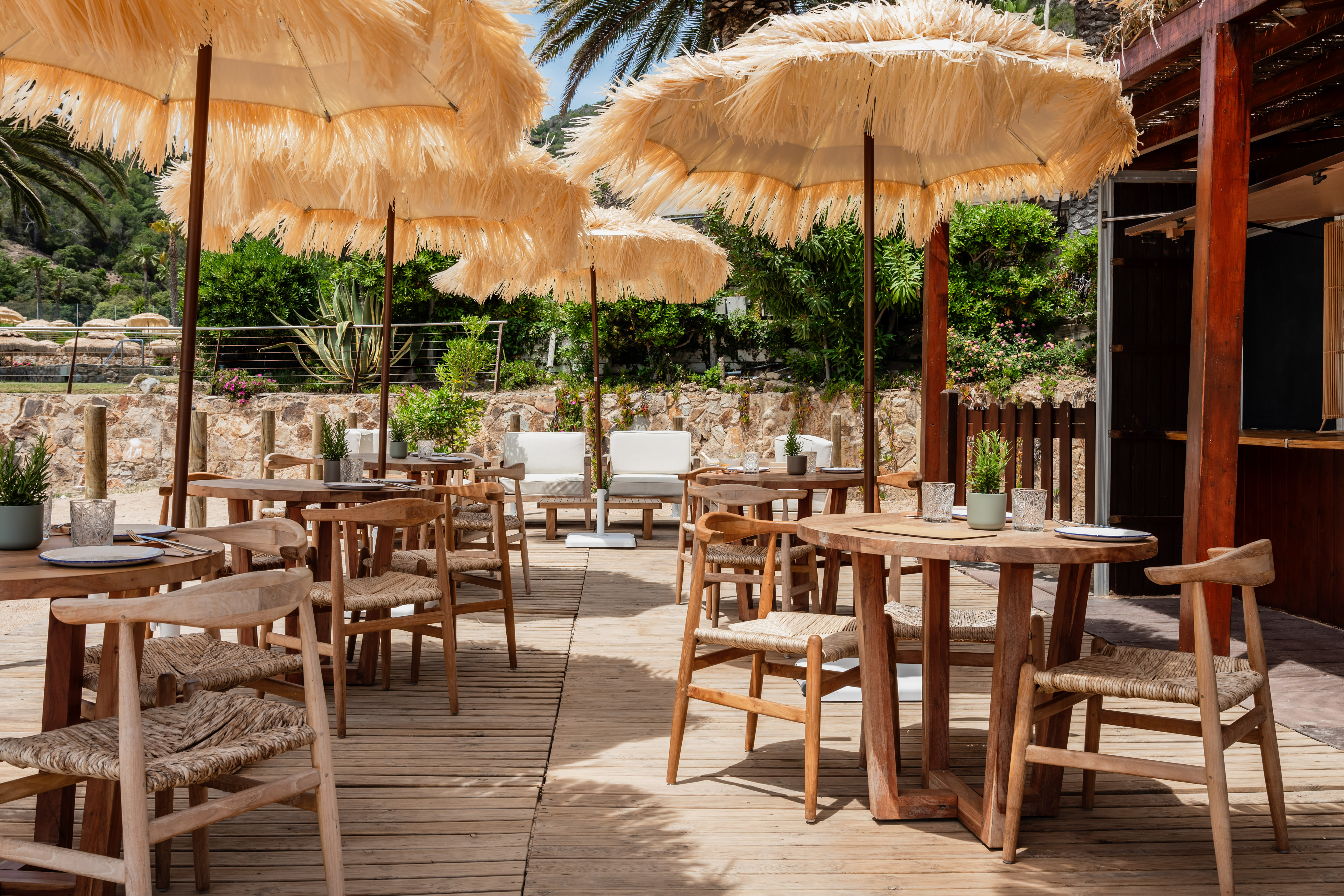 Beach cafe terrace with straw umbrellas, wooden tables, and woven chairs.