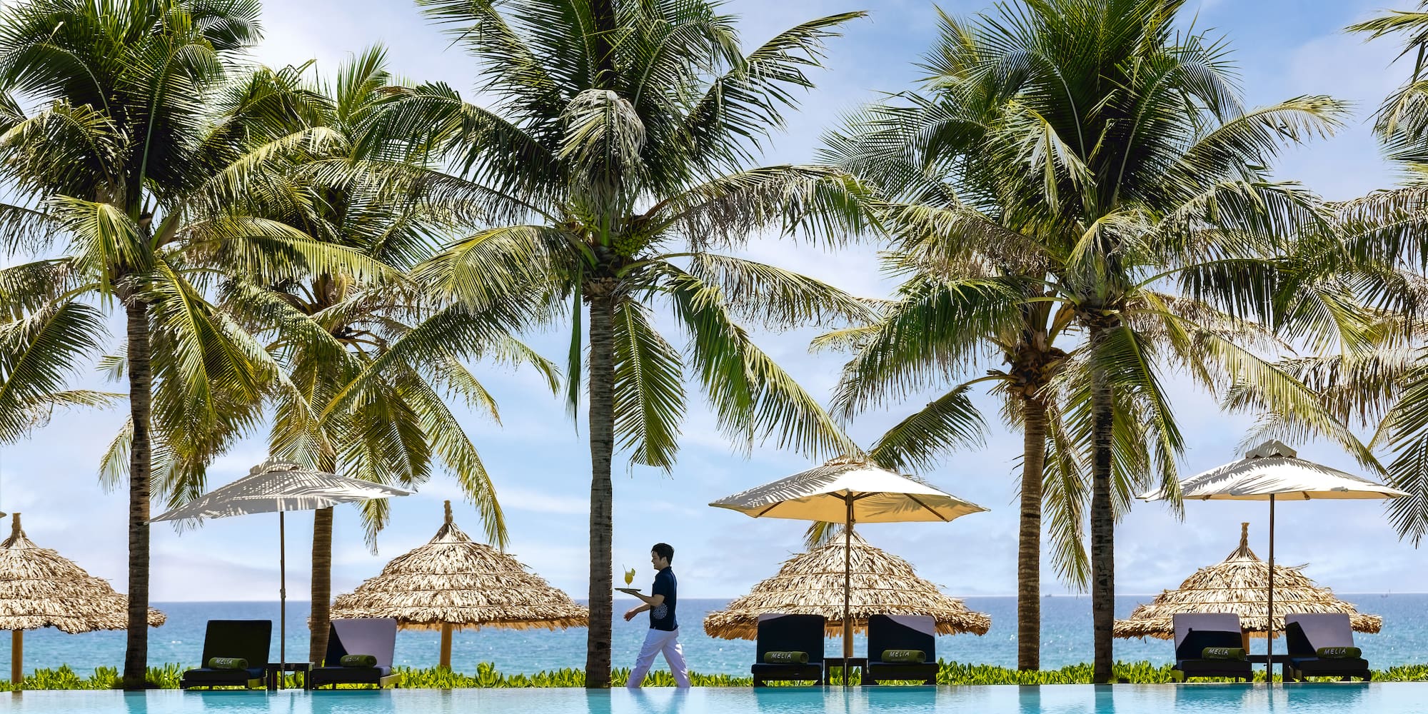 a person standing next to a pool with umbrellas and palm trees
