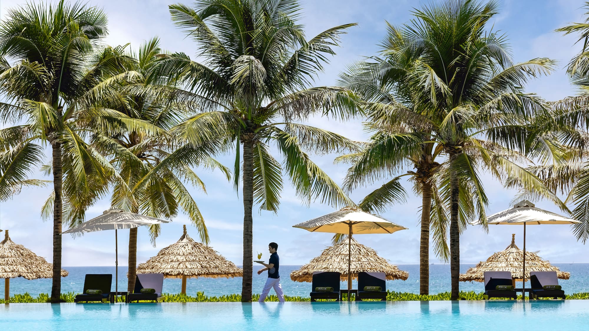 a person standing next to a pool with umbrellas and palm trees