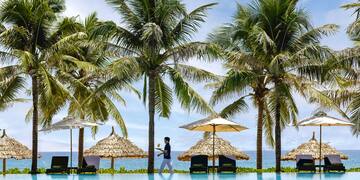 a person standing next to a pool with umbrellas and palm trees