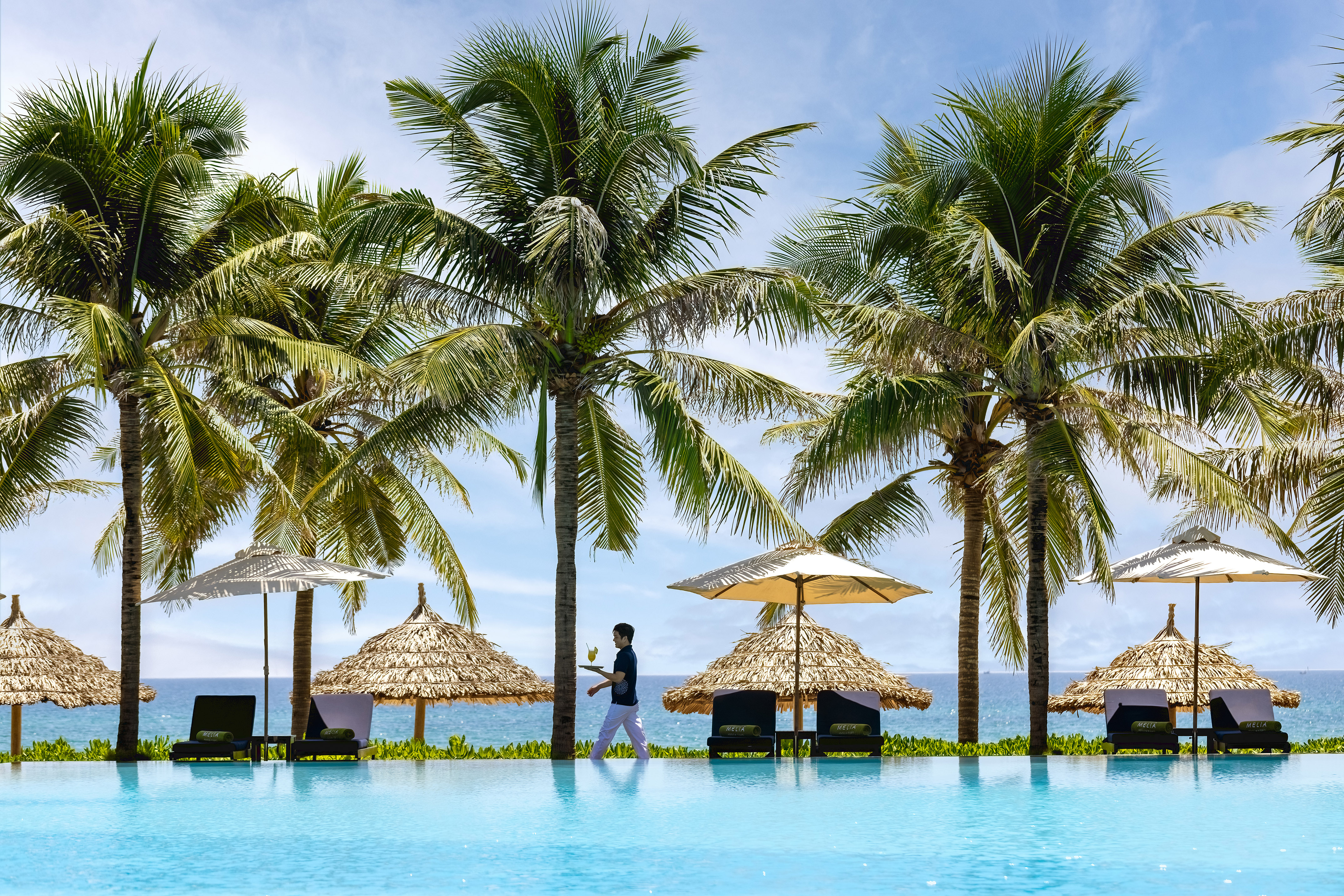 a person standing next to a pool with umbrellas and palm trees