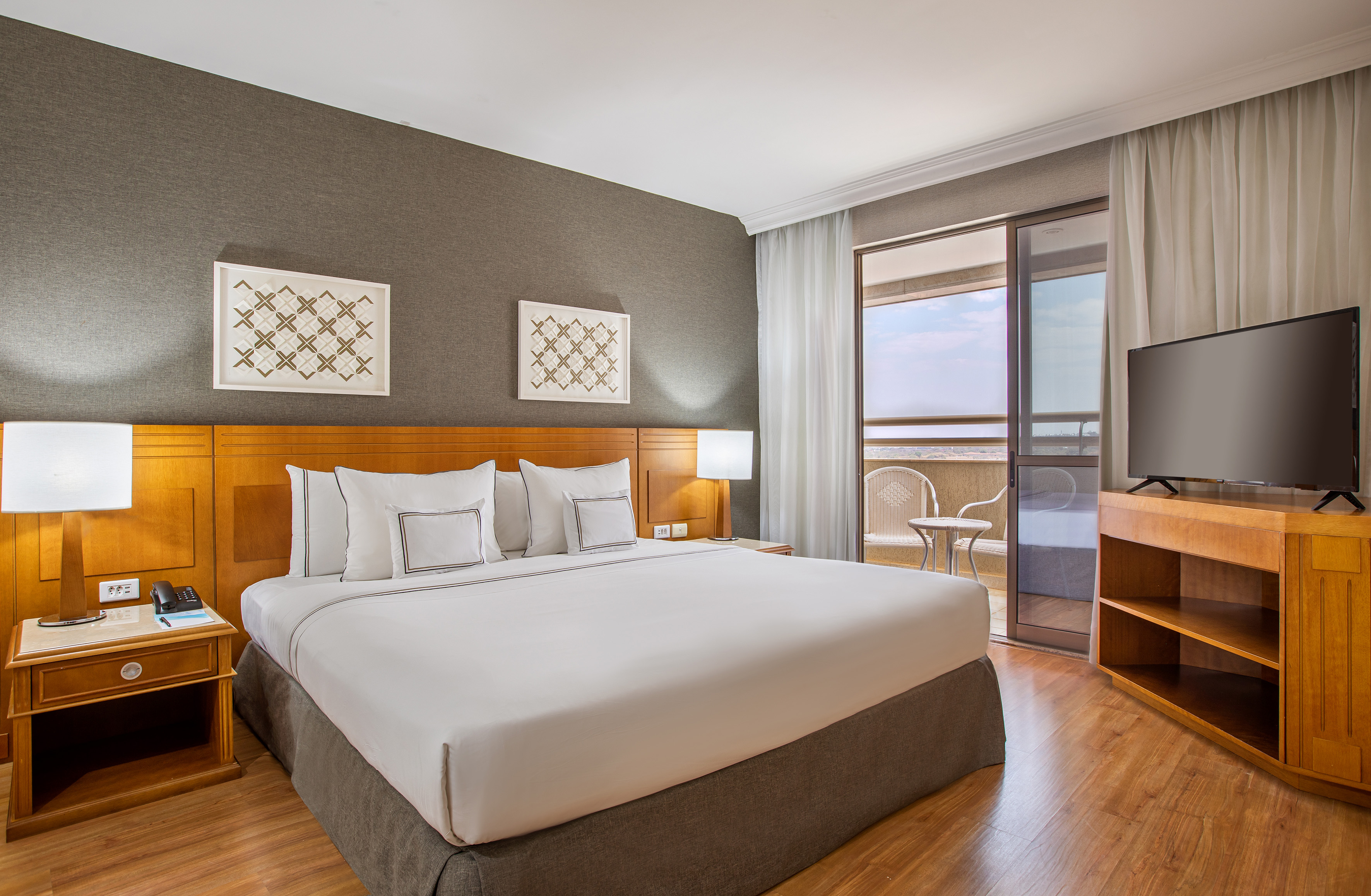 Modern hotel bedroom with king bed, balcony, and flat-screen TV.