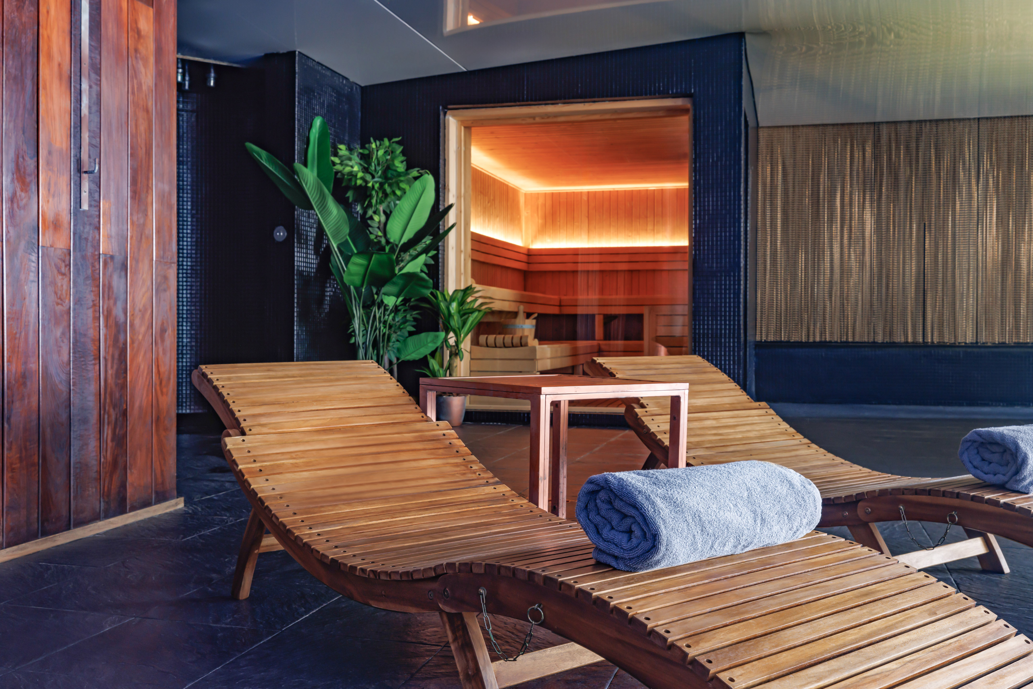 Modern wellness spa with wooden lounge chairs, blue towels, and a warm sauna.