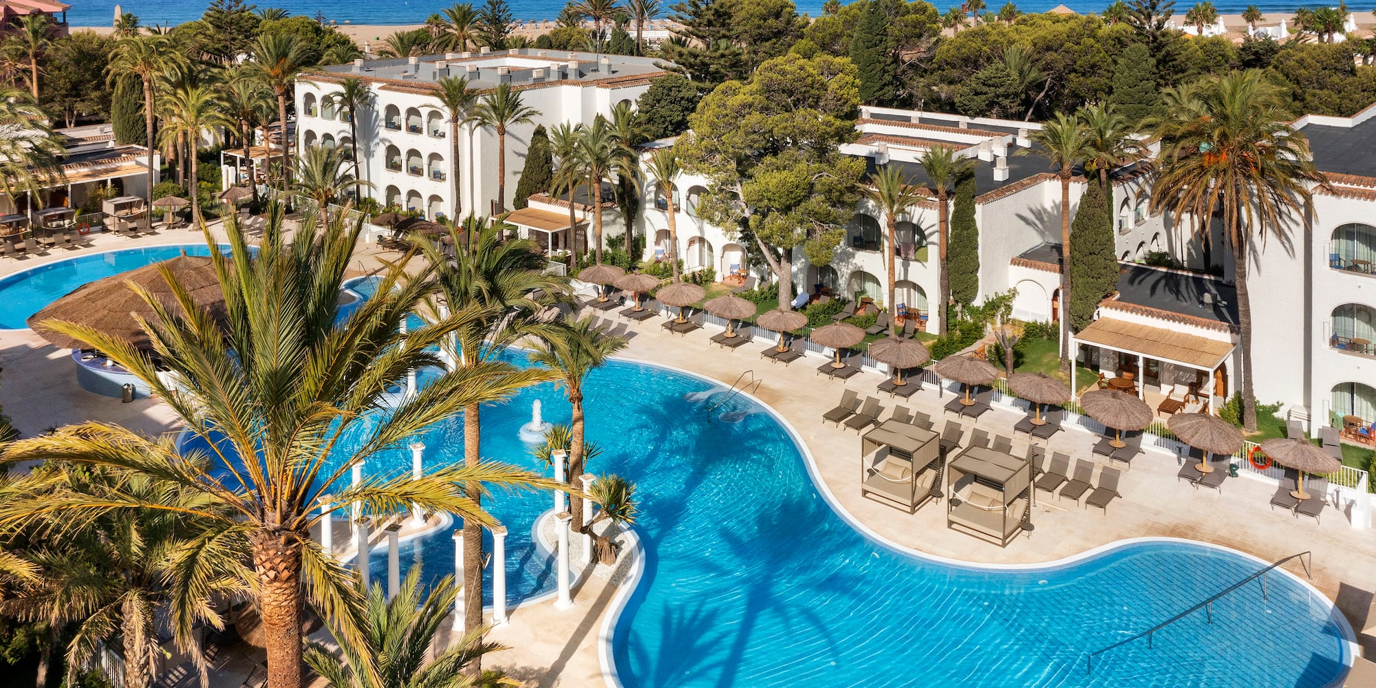 a swimming pool with palm trees and a building with a beach and blue sky
