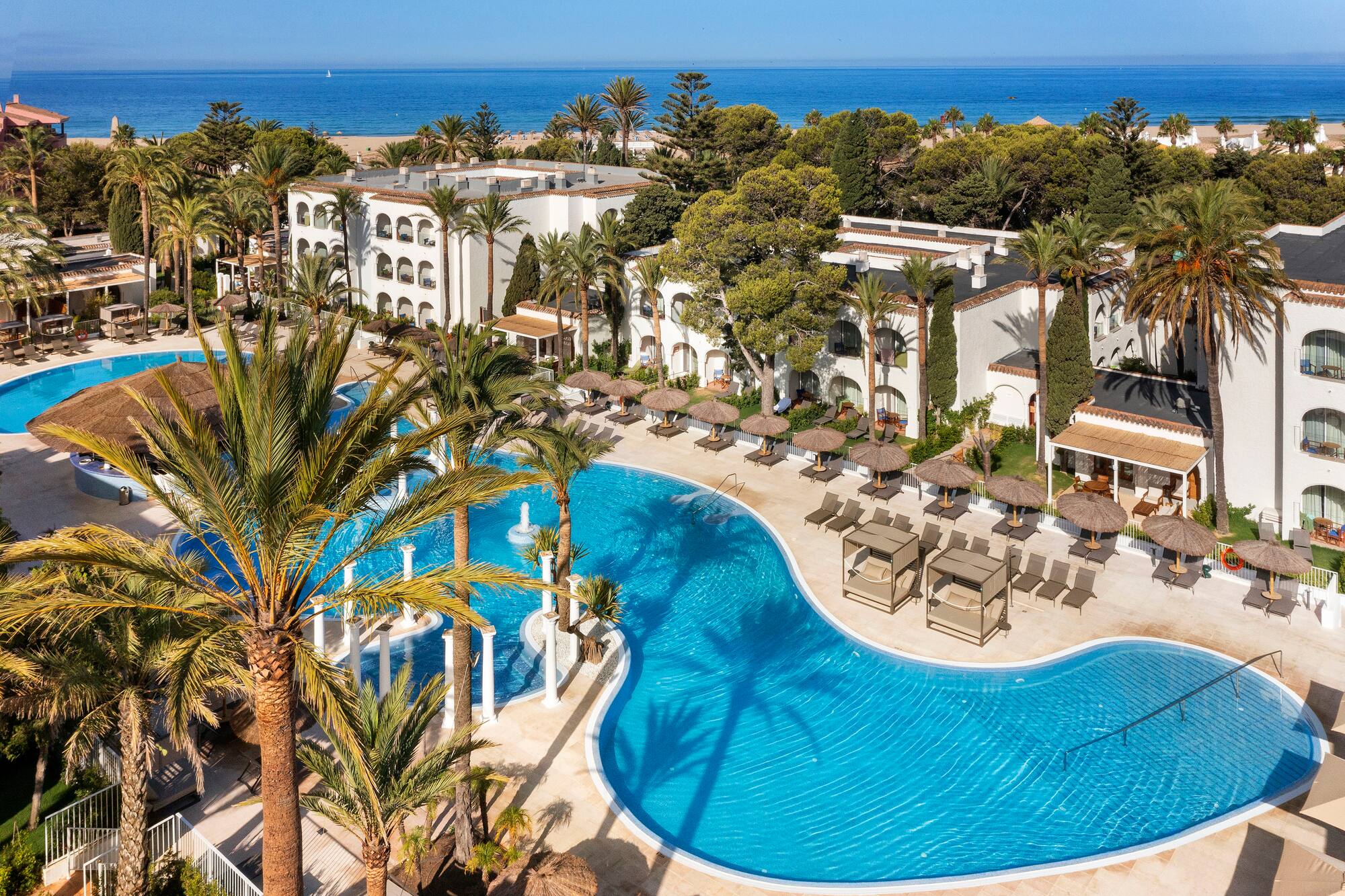 a swimming pool with palm trees and a building with a beach and blue sky