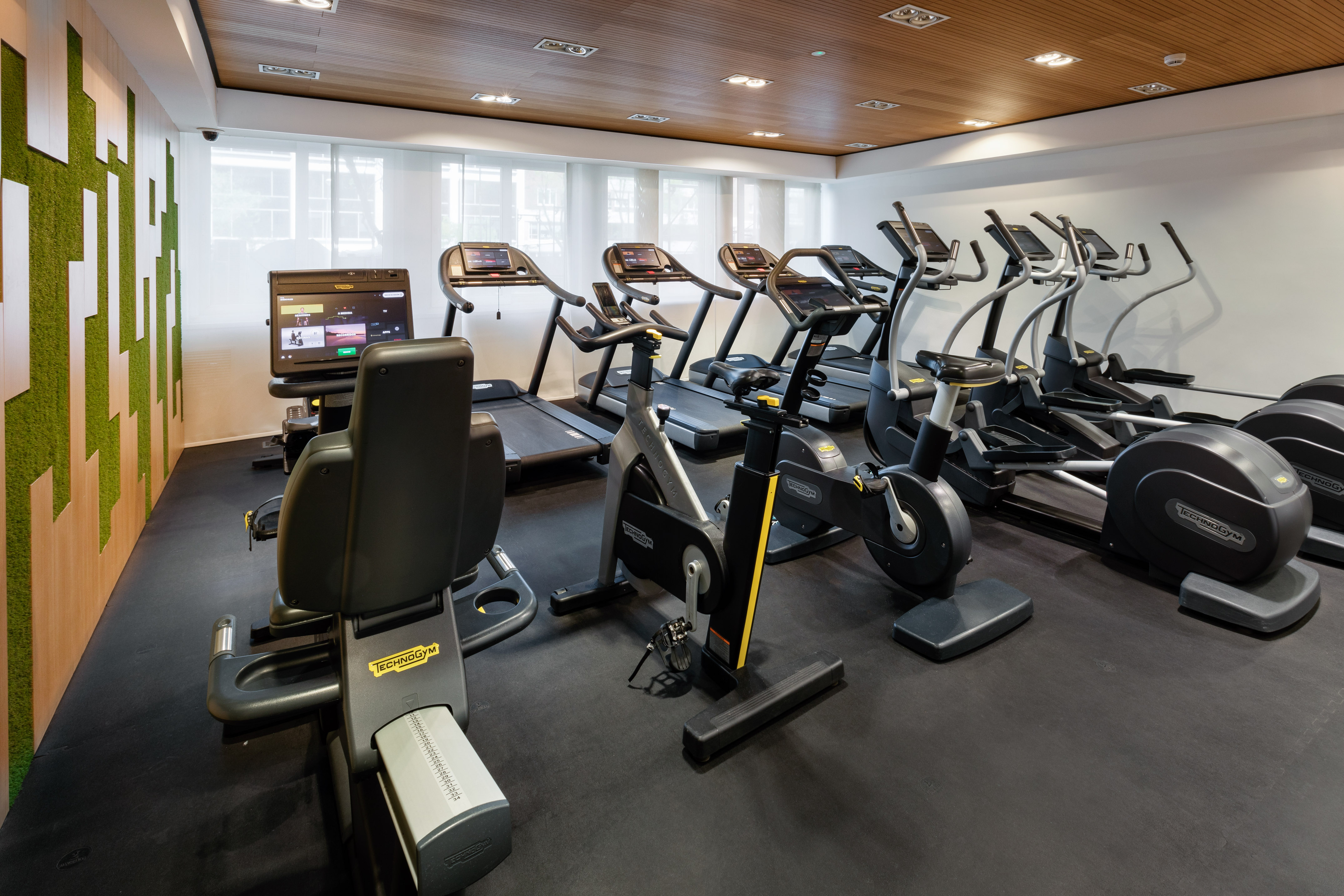 Modern gym with Technogym treadmills, bikes, ellipticals, and green wall.