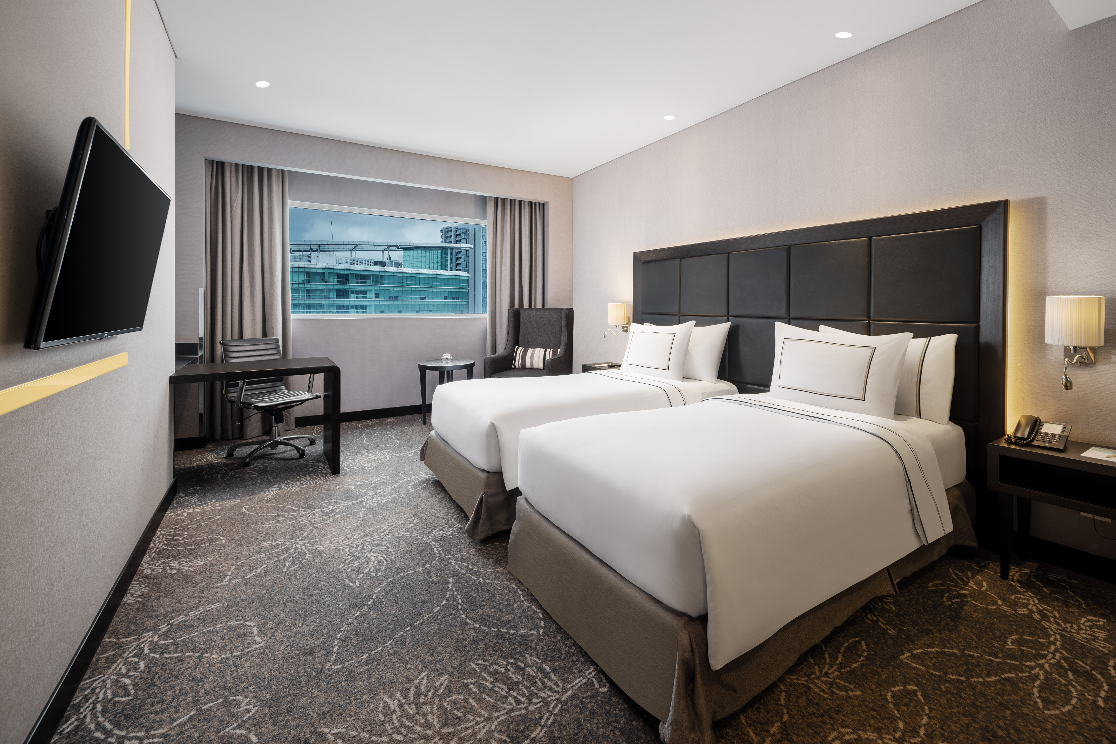 Contemporary twin bedroom with city view, desk, and TV.