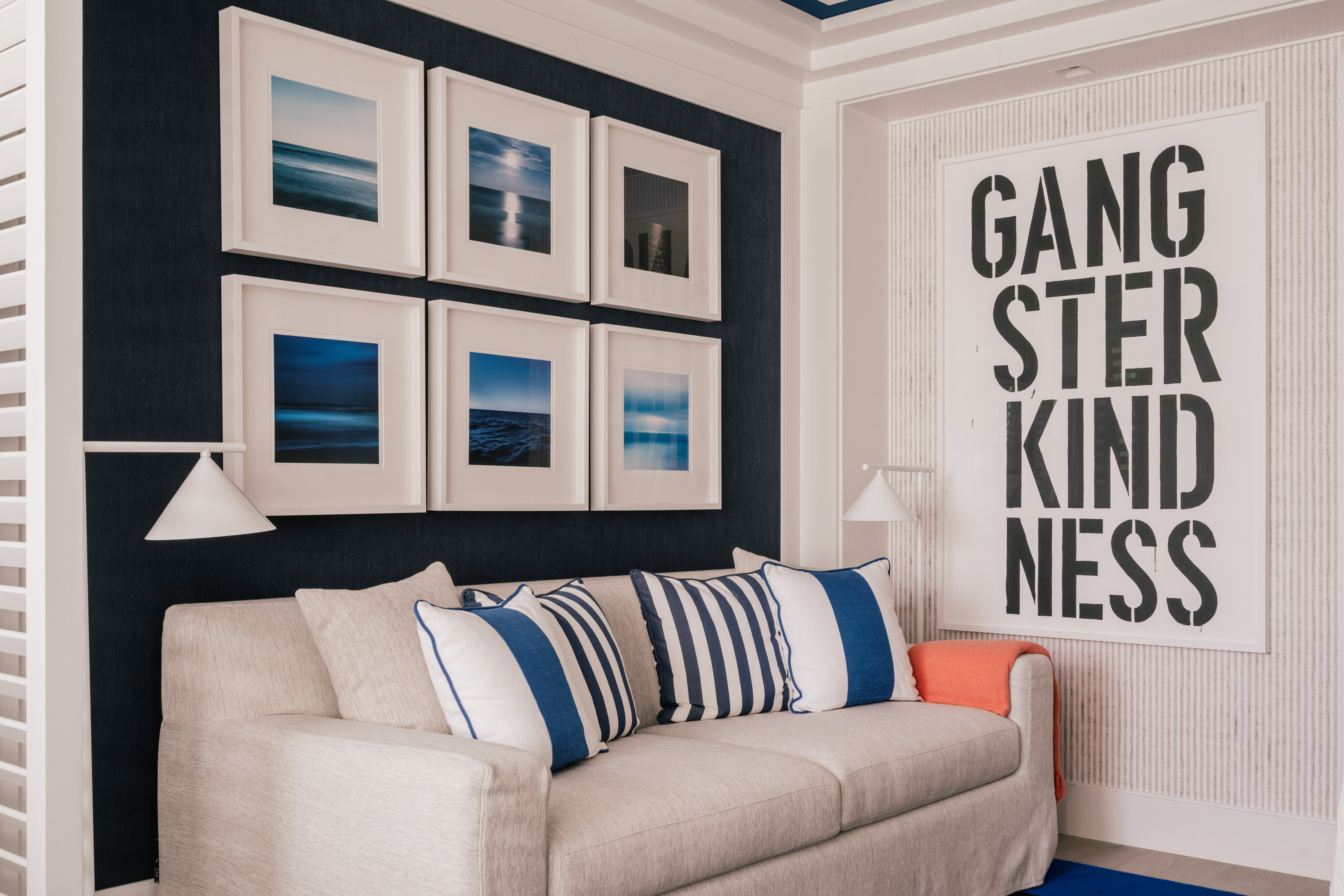 Nautical living room with beige sofa, blue pillows, ocean art, navy wall.