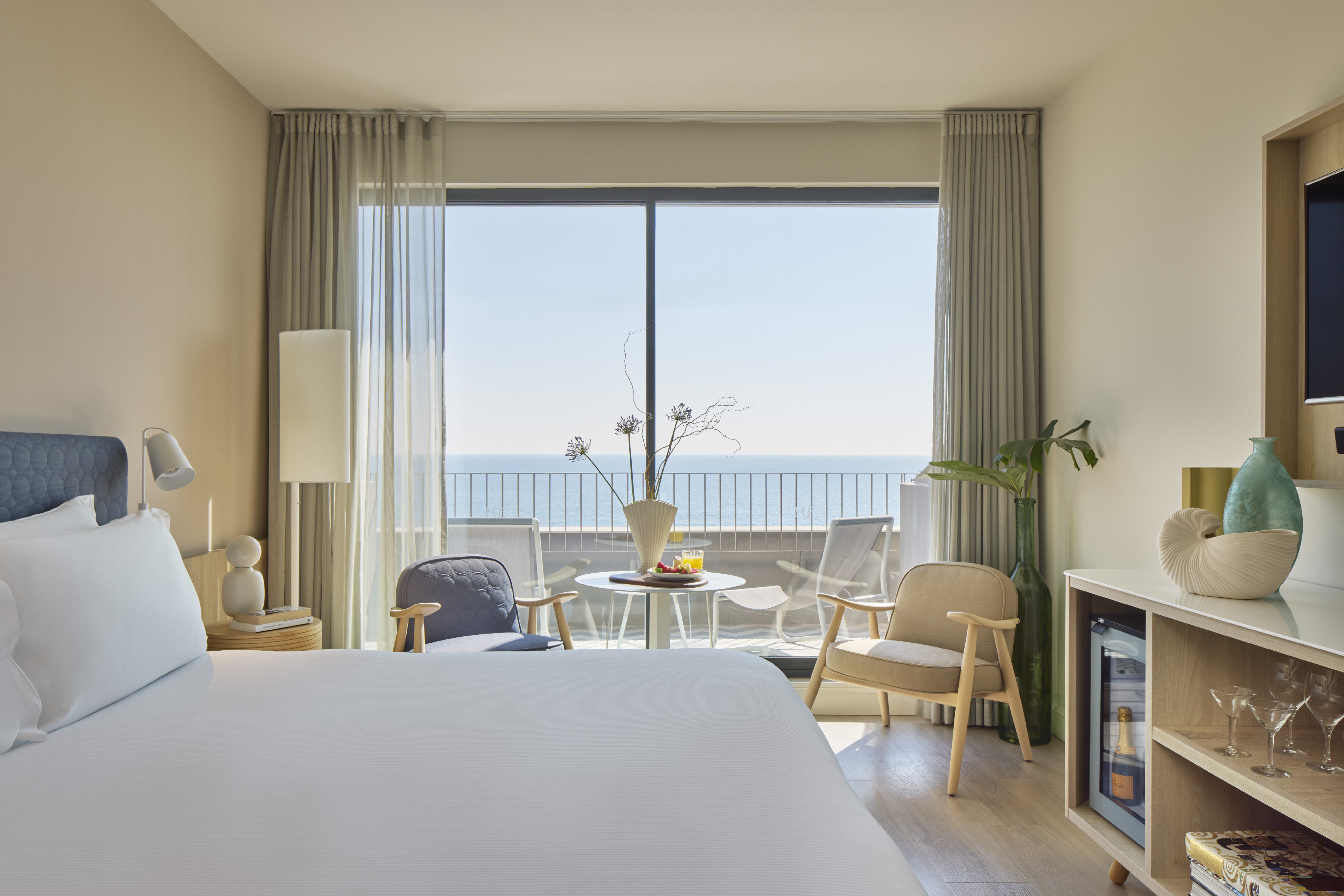 Bright hotel room with ocean view balcony, large bed, and modern furniture.