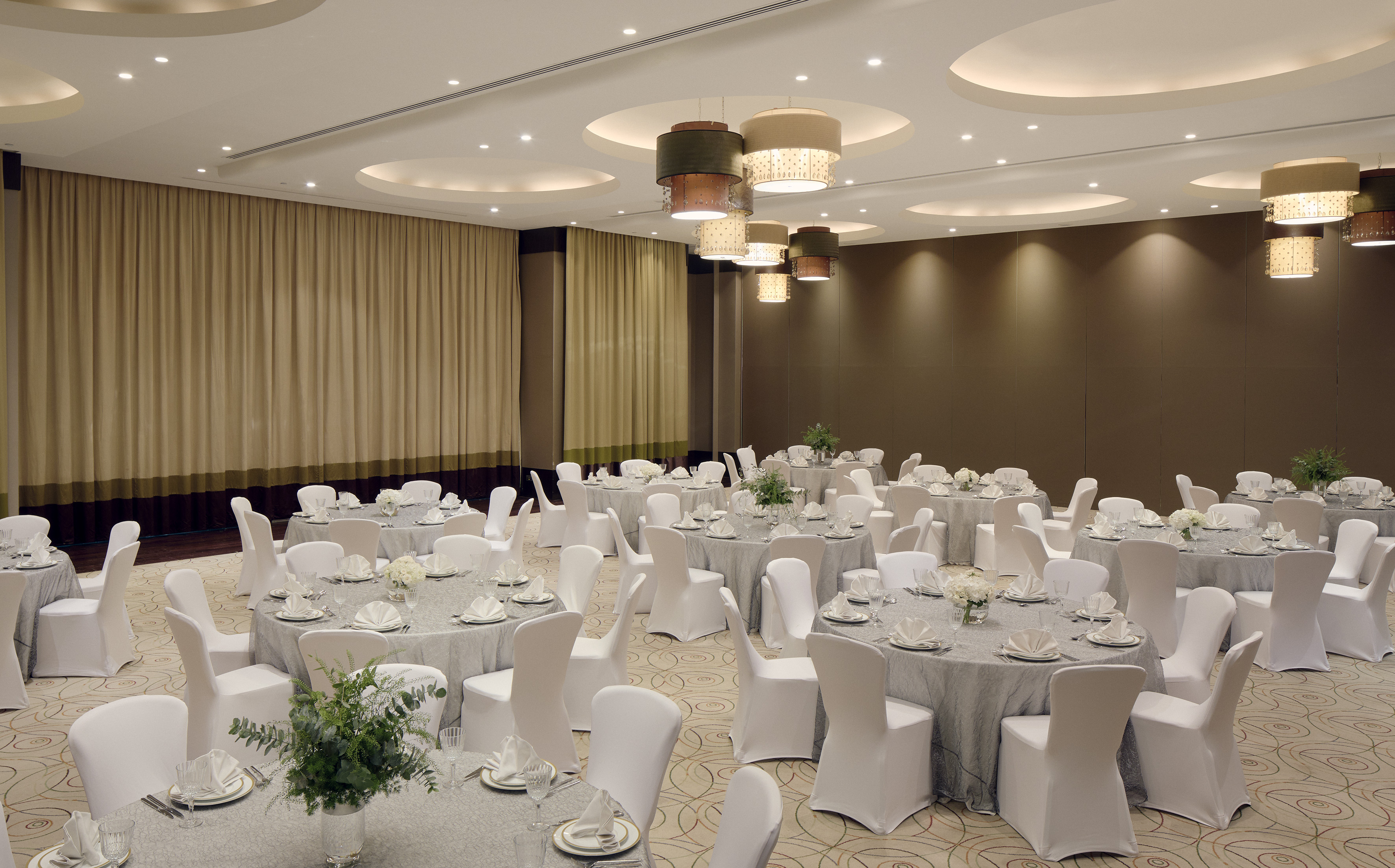 Spacious hotel ballroom set with round tables, white chairs, and modern lighting.