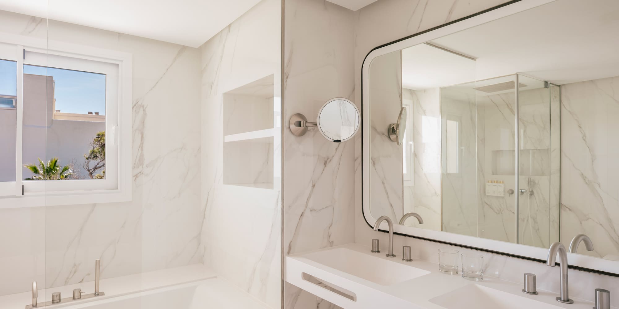Modern hotel bathroom with marble, double vanity, bathtub, and large mirror.