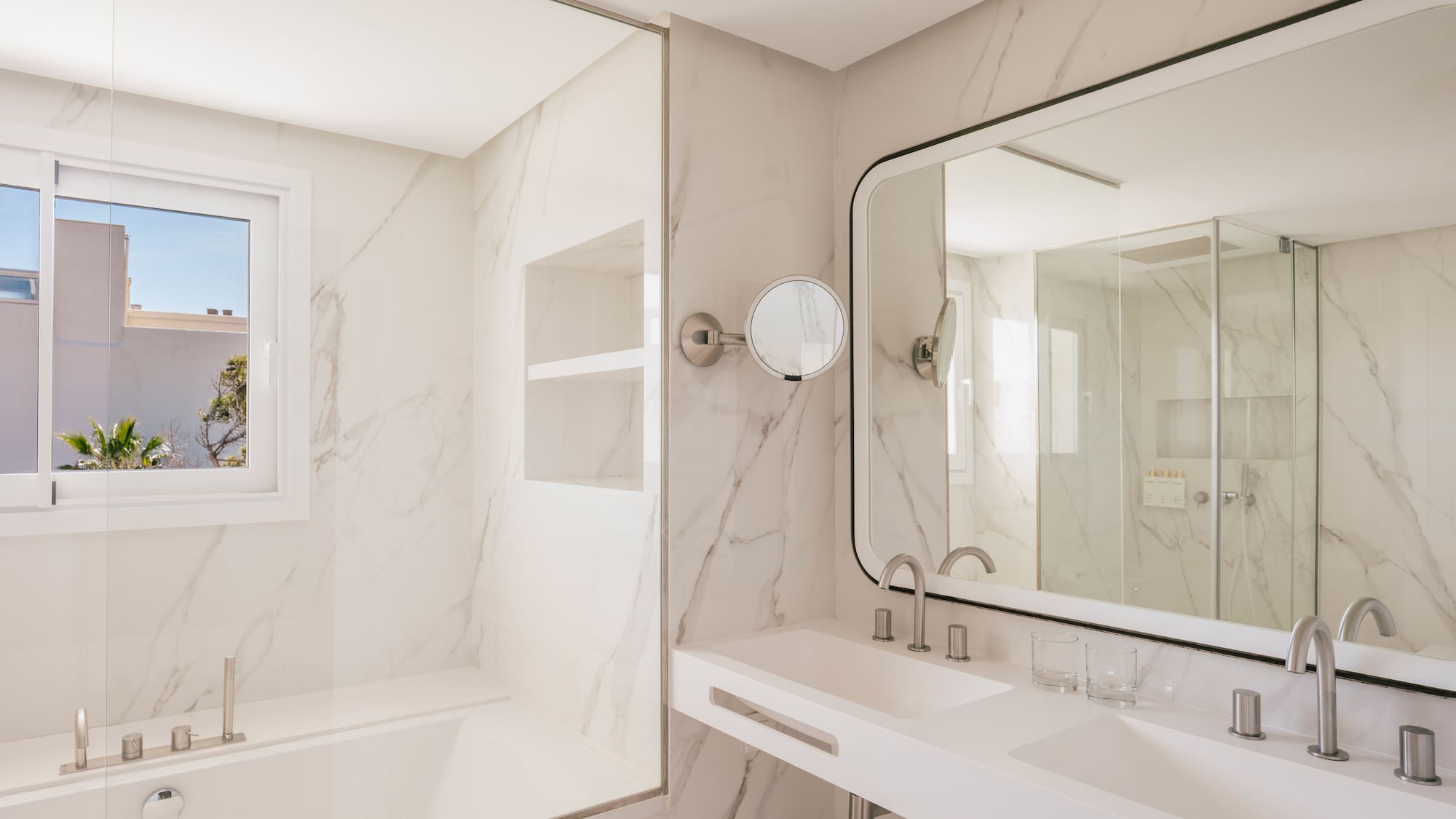 Modern hotel bathroom with marble, double vanity, bathtub, and large mirror.