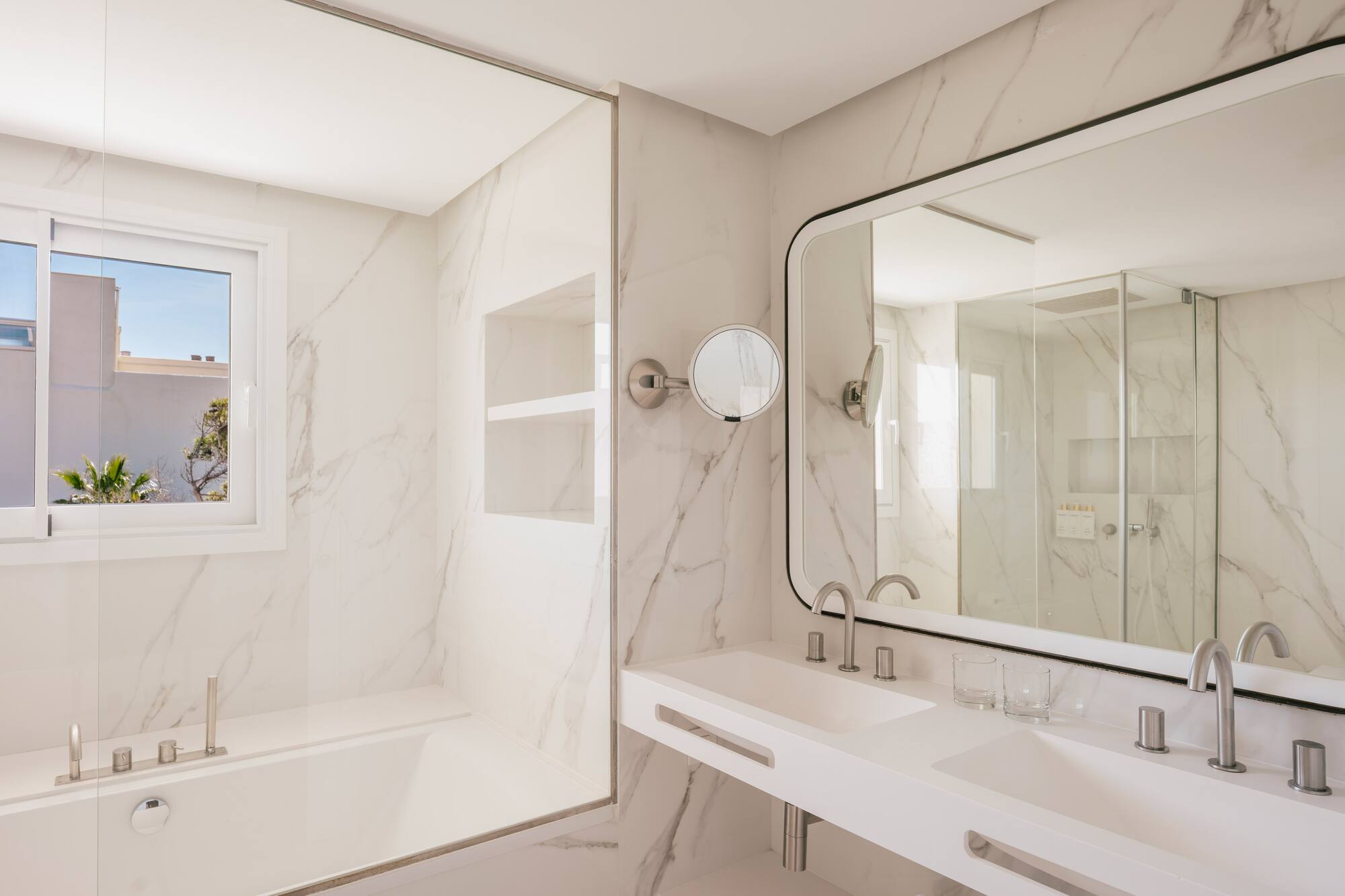 Baño lujoso de hotel, mármol blanco, bañera, doble lavabo, ducha.