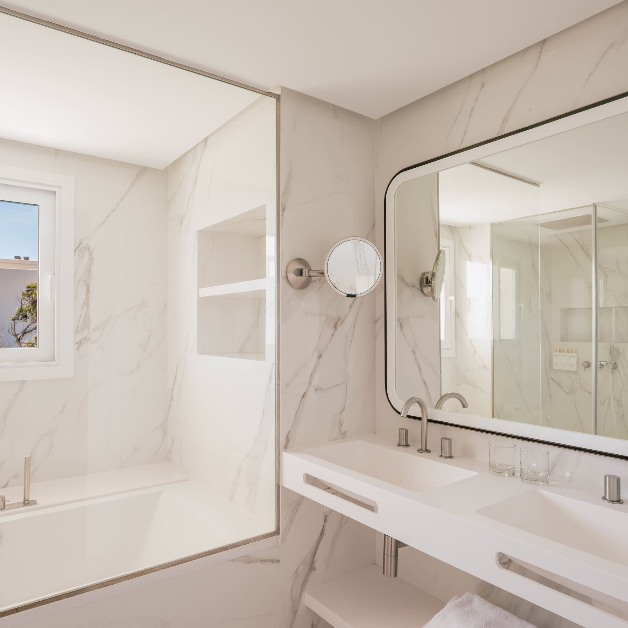 Modern hotel bathroom with marble, double vanity, bathtub, and large mirror.