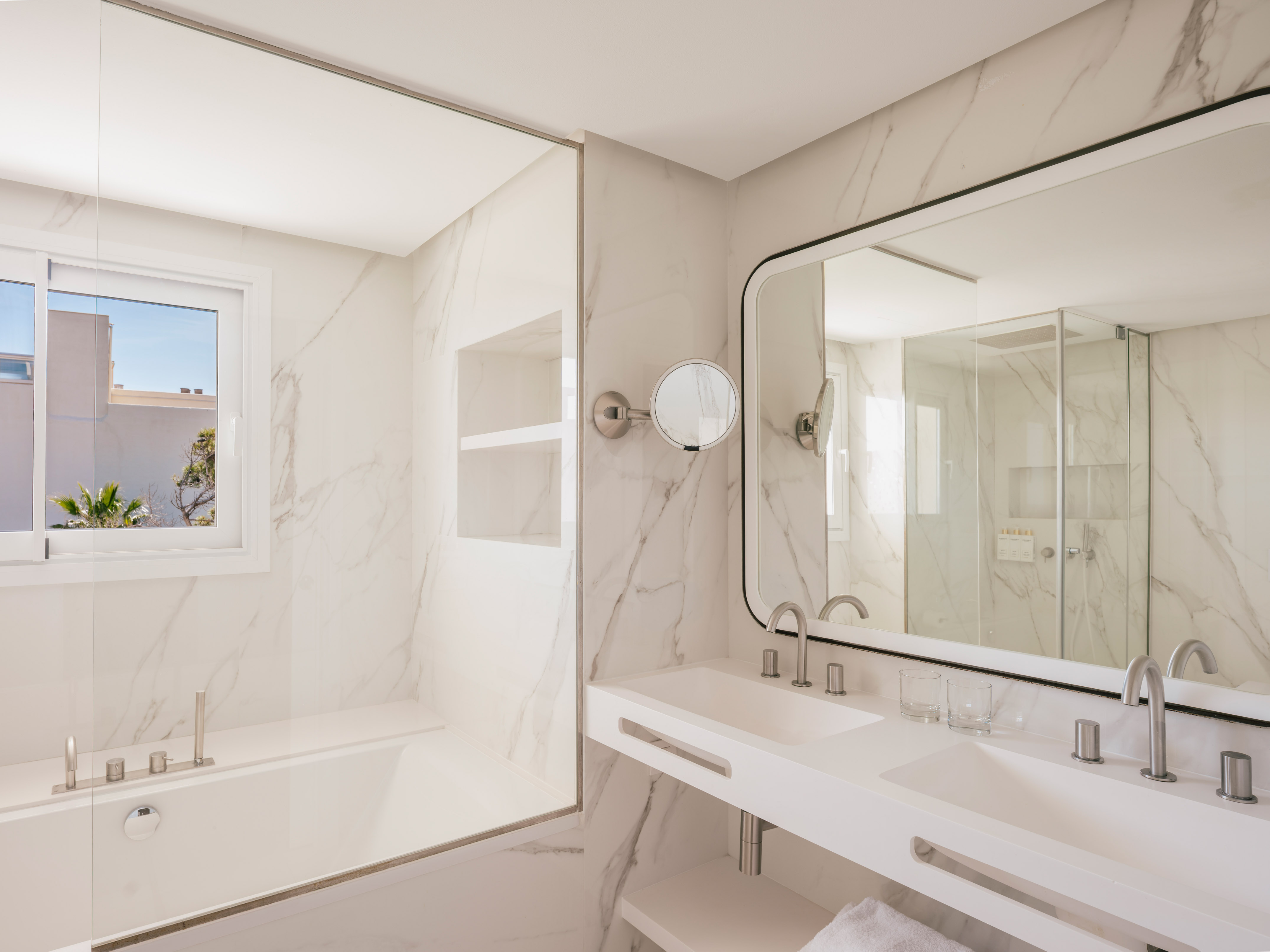 Modern hotel bathroom with marble, double vanity, bathtub, and large mirror.