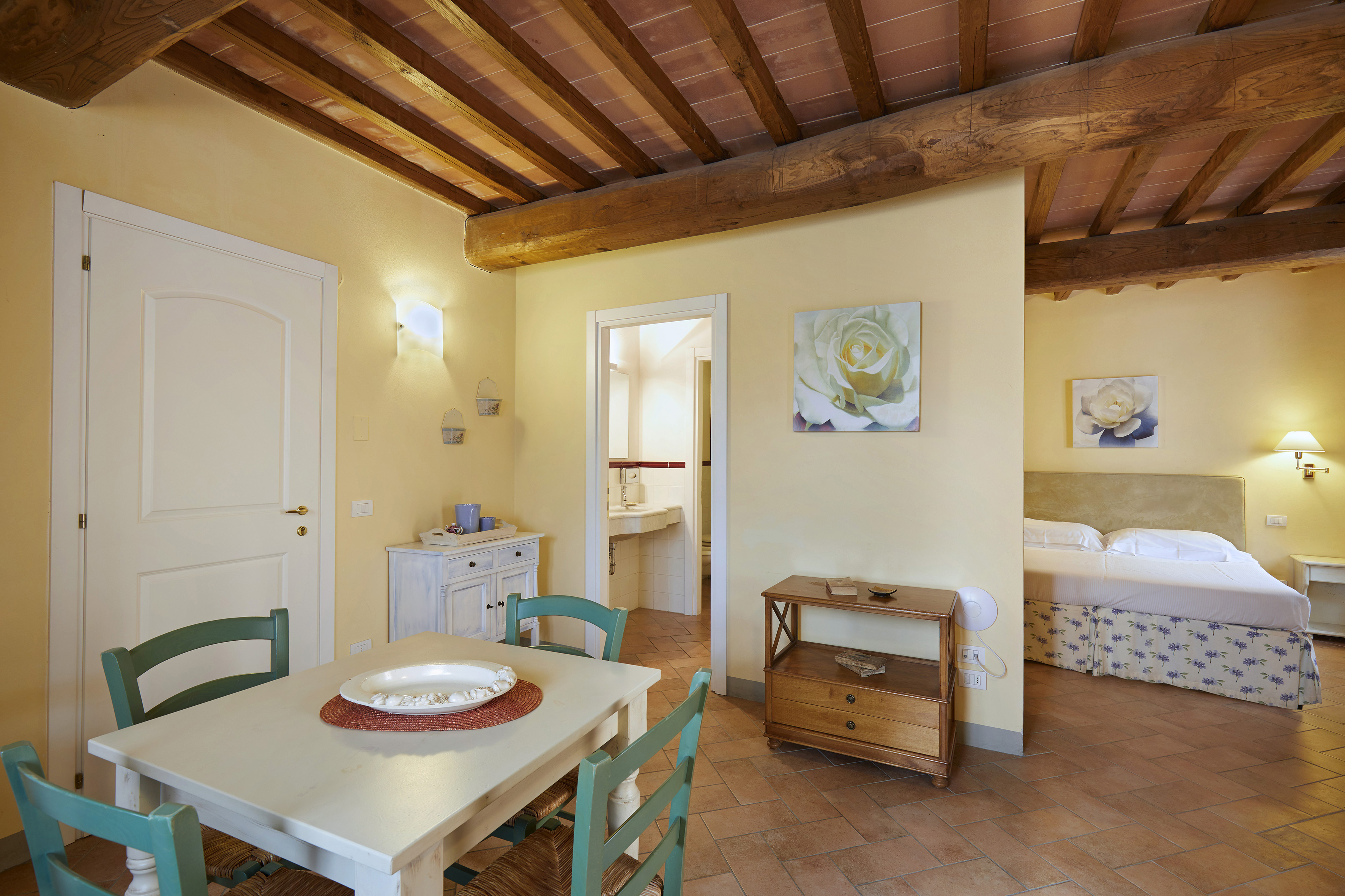 Tuscan apartment: dining, bedroom, terracotta floors, exposed wood beams.