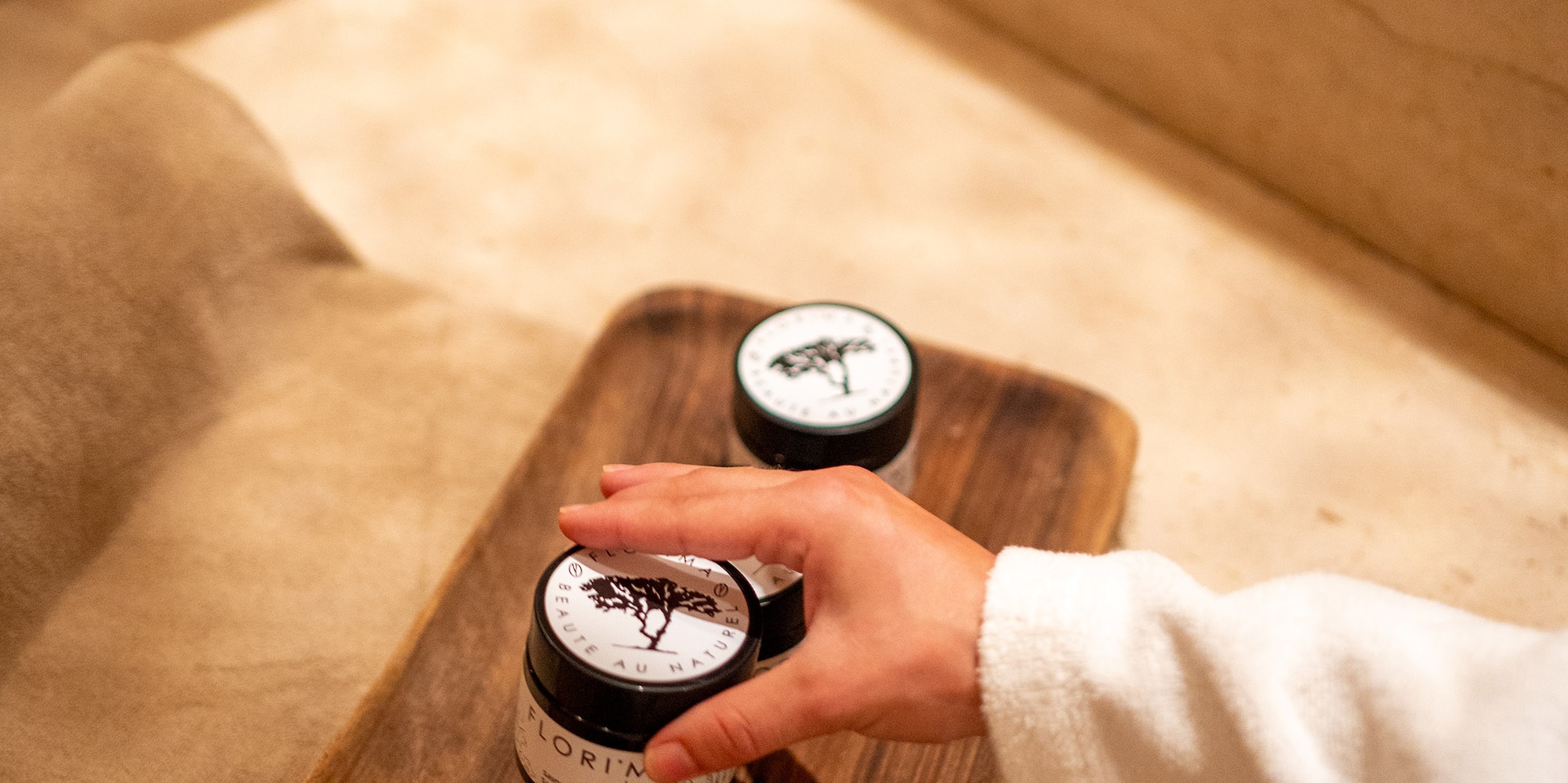 a person touching a jar of cream on a wooden tray