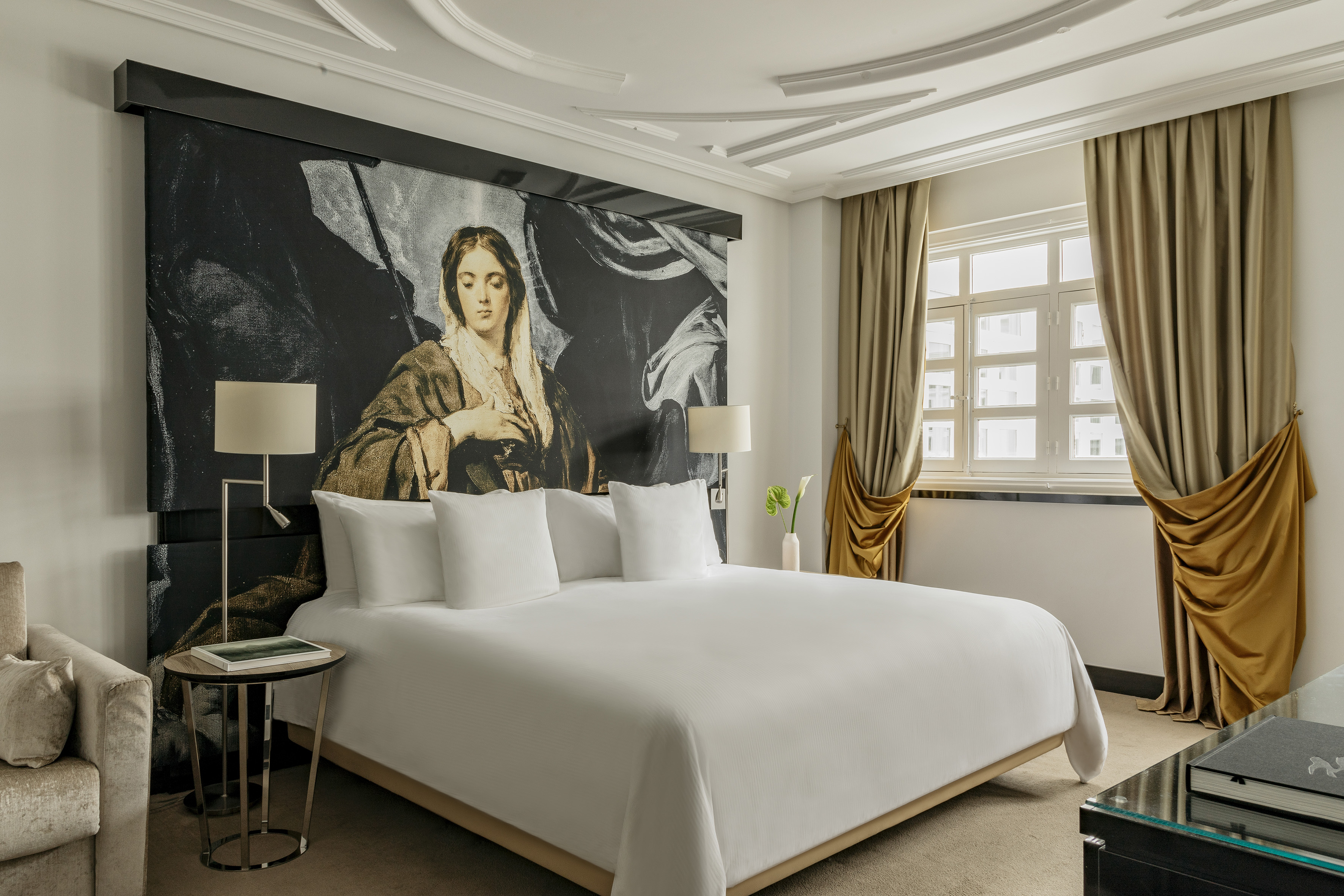 Elegant hotel bedroom with king bed, classic artwork headboard, and gold curtains.