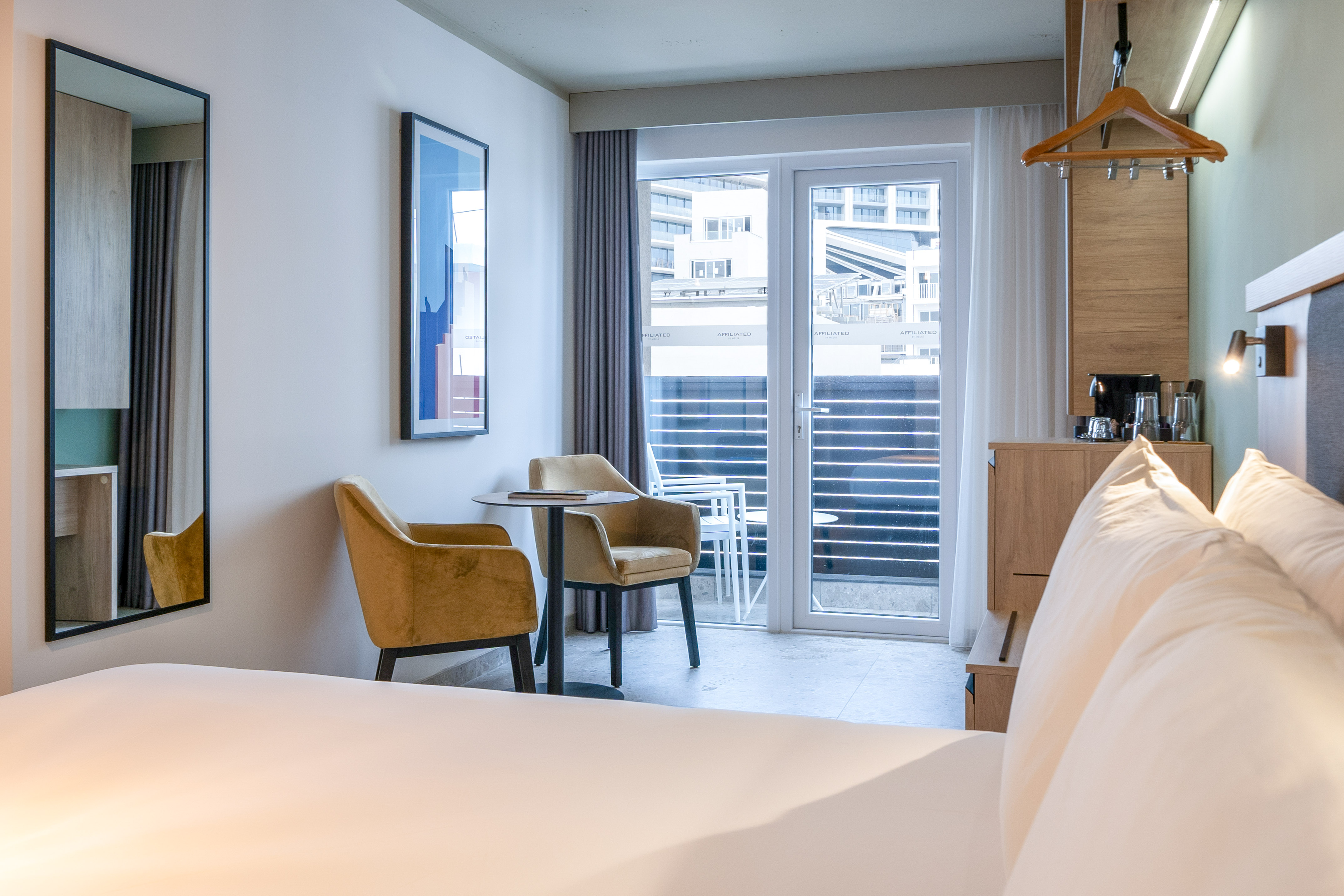 Contemporary hotel room with bed, yellow seating, balcony, and coffee maker.