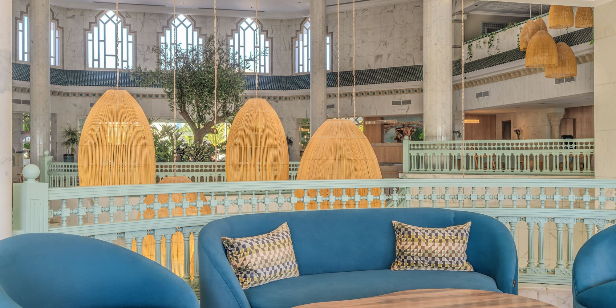 Luxury hotel lounge with blue sofas, wooden table, and wicker hanging lights.