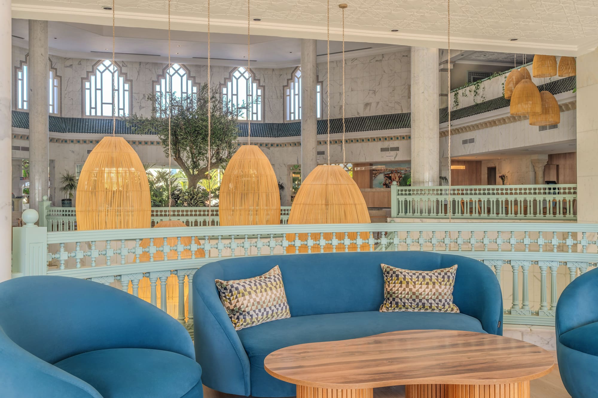 Luxury hotel lounge with blue sofas, wooden table, and wicker hanging lights.