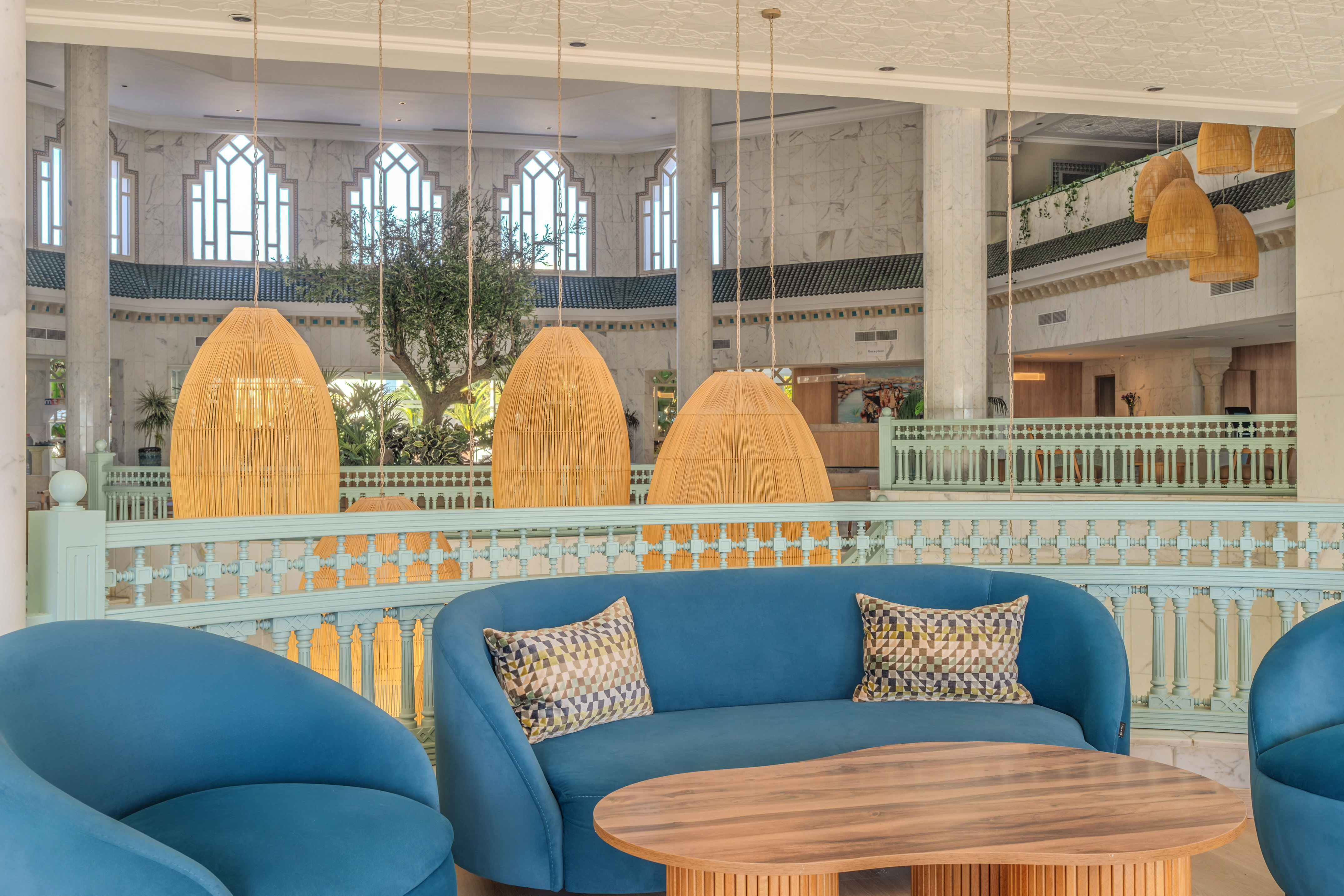 Luxury hotel lounge with blue sofas, wooden table, and wicker hanging lights.