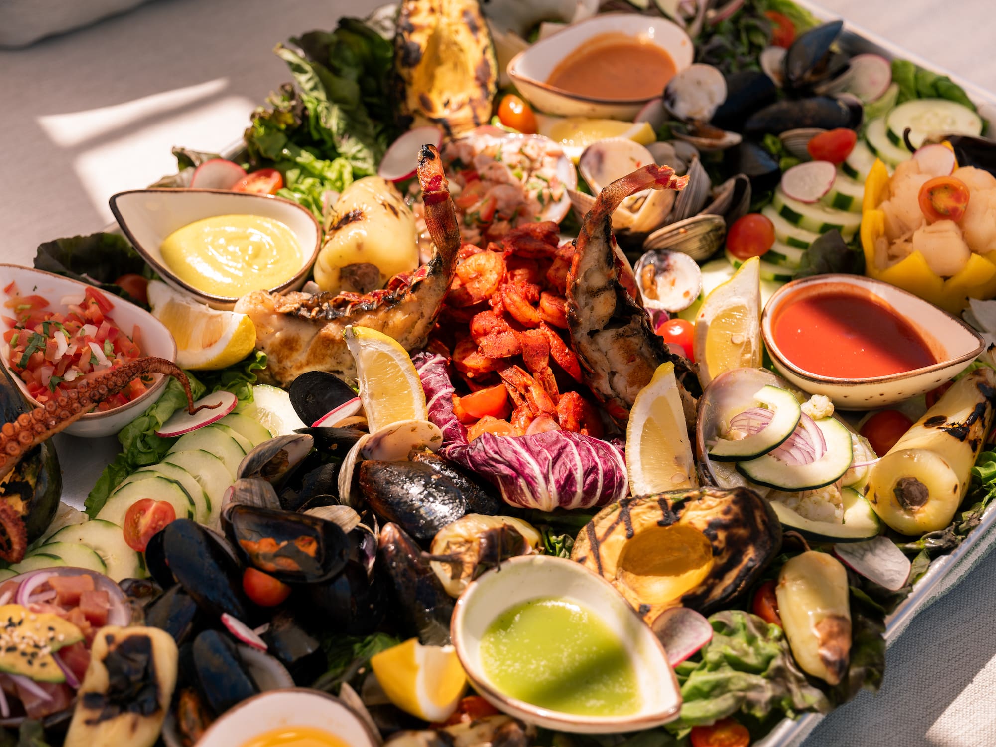 a plate of seafood with sauces and vegetables
