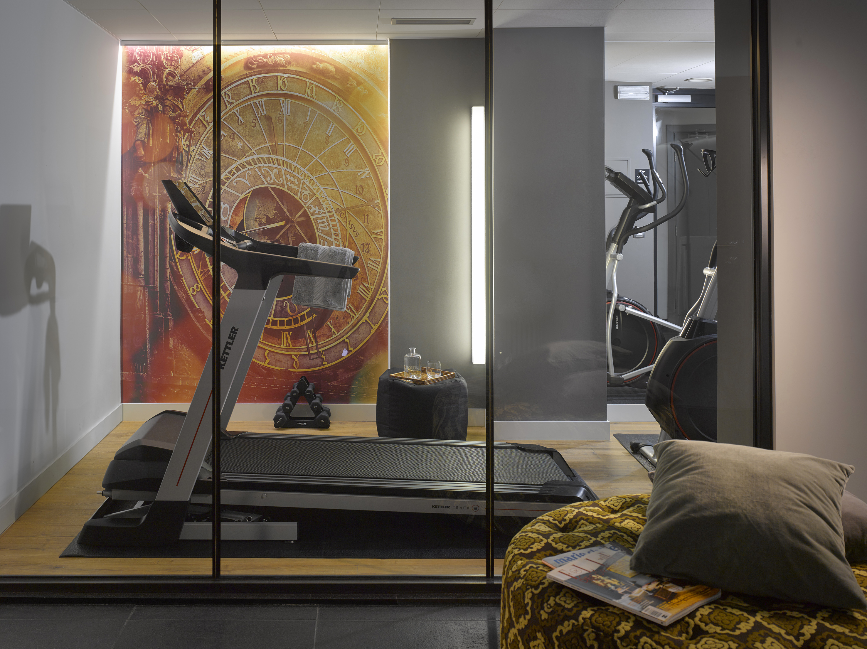 Home gym with treadmill, elliptical, dumbbells, and decorative clock mural.