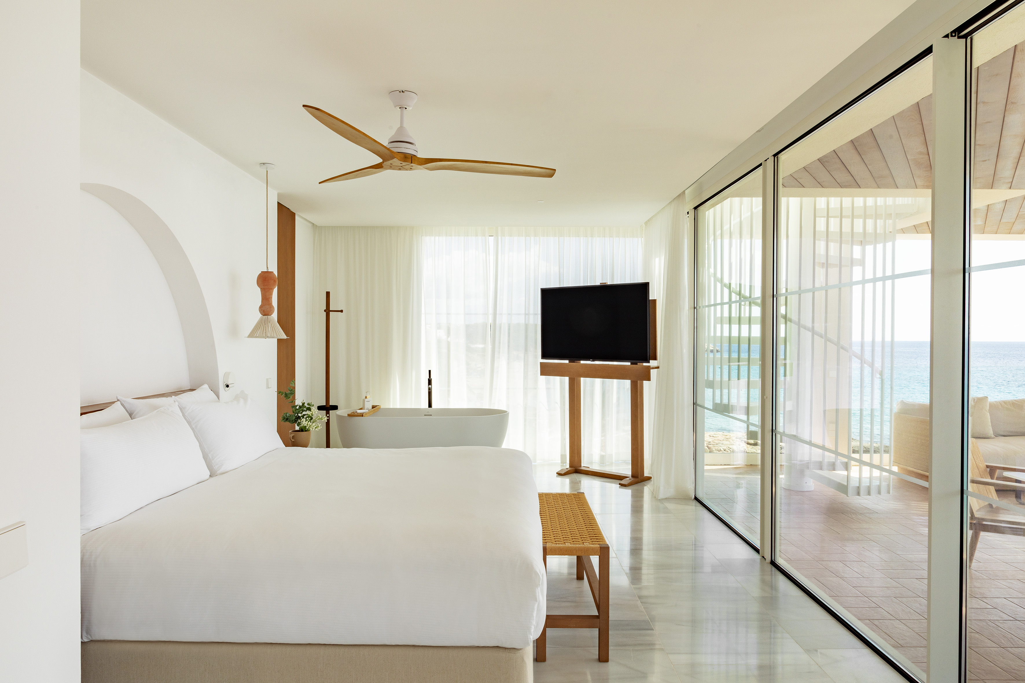 Bright hotel bedroom with ocean view, bed, freestanding tub, and modern design.